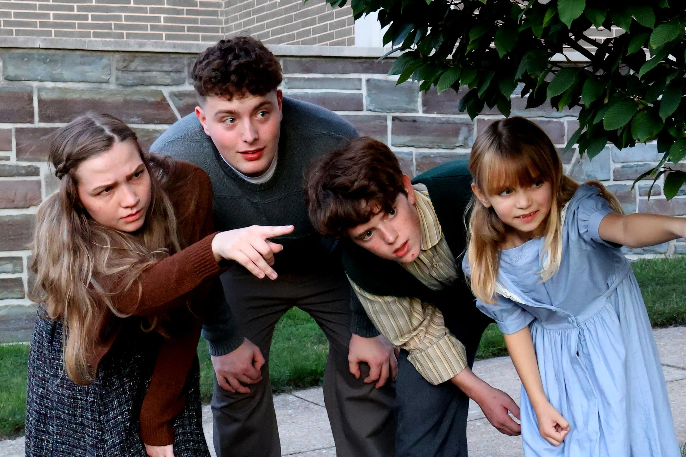 Show photo from The Lion, the Witch, and the Wardrobe. A group of 4 children peering around a bush and one girl is pointing at something off camera.