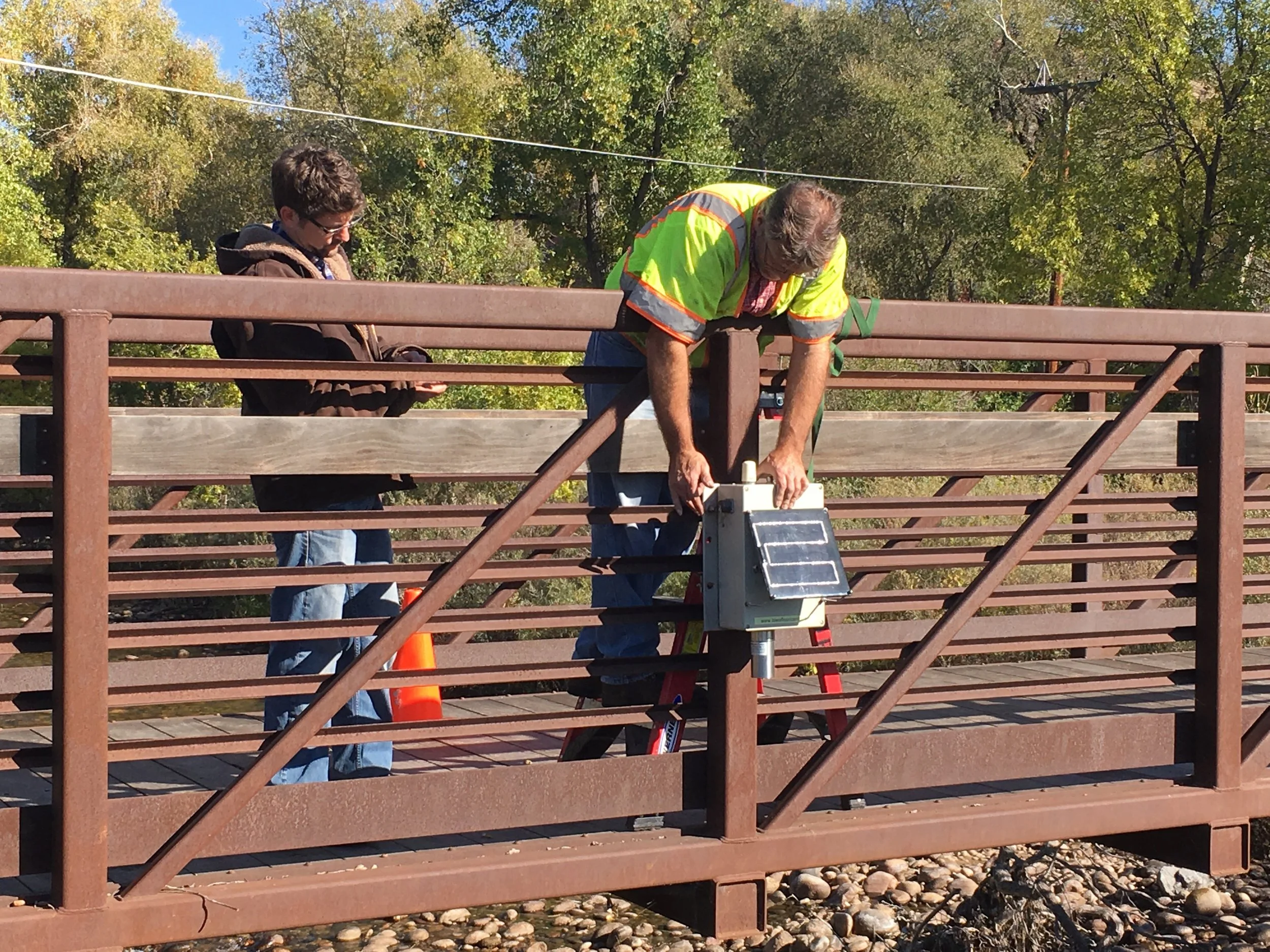 Sean McFeely (left) Product Manager for RiverTrak, assists Dan Ceynar (right) of Iowa Flood Center to install a Sensor on the Poudre River near Bellvue.