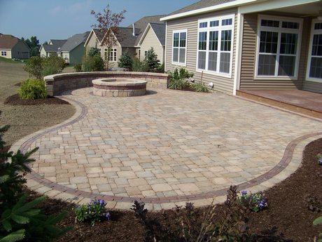 Backyard patio made with brick pavers, a built-in circular fire pit, and bult-in brick seating the stretches half way around the fire pit.