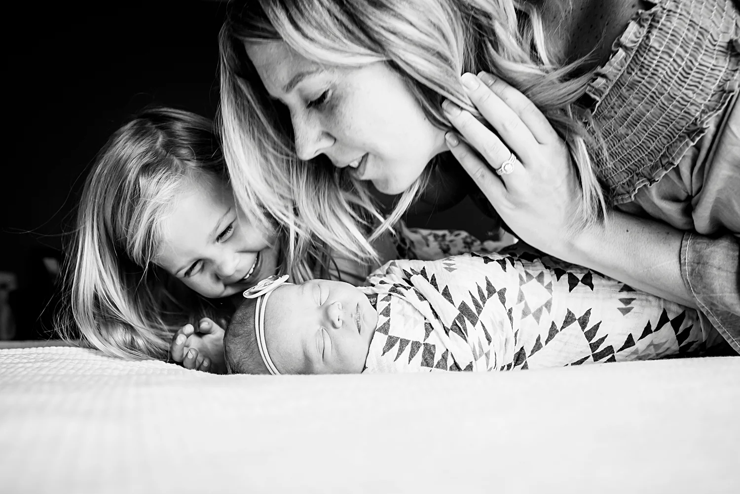 Three girls--a mom and new big sister gaze at a newborn baby girl during a photo shoot in Highlands Ranch, Colorado, with Kristiina Craven Photography.