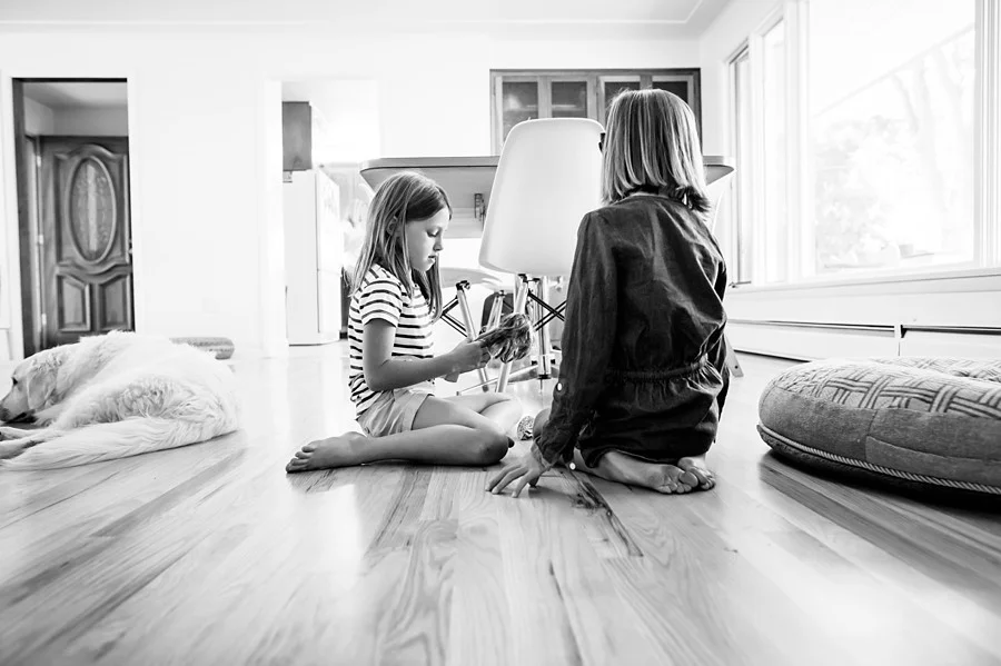 Two young girls play Barbie while their dog rests nearby in this black and white image by Kristiina Craven Photography in Denver, Colorado.