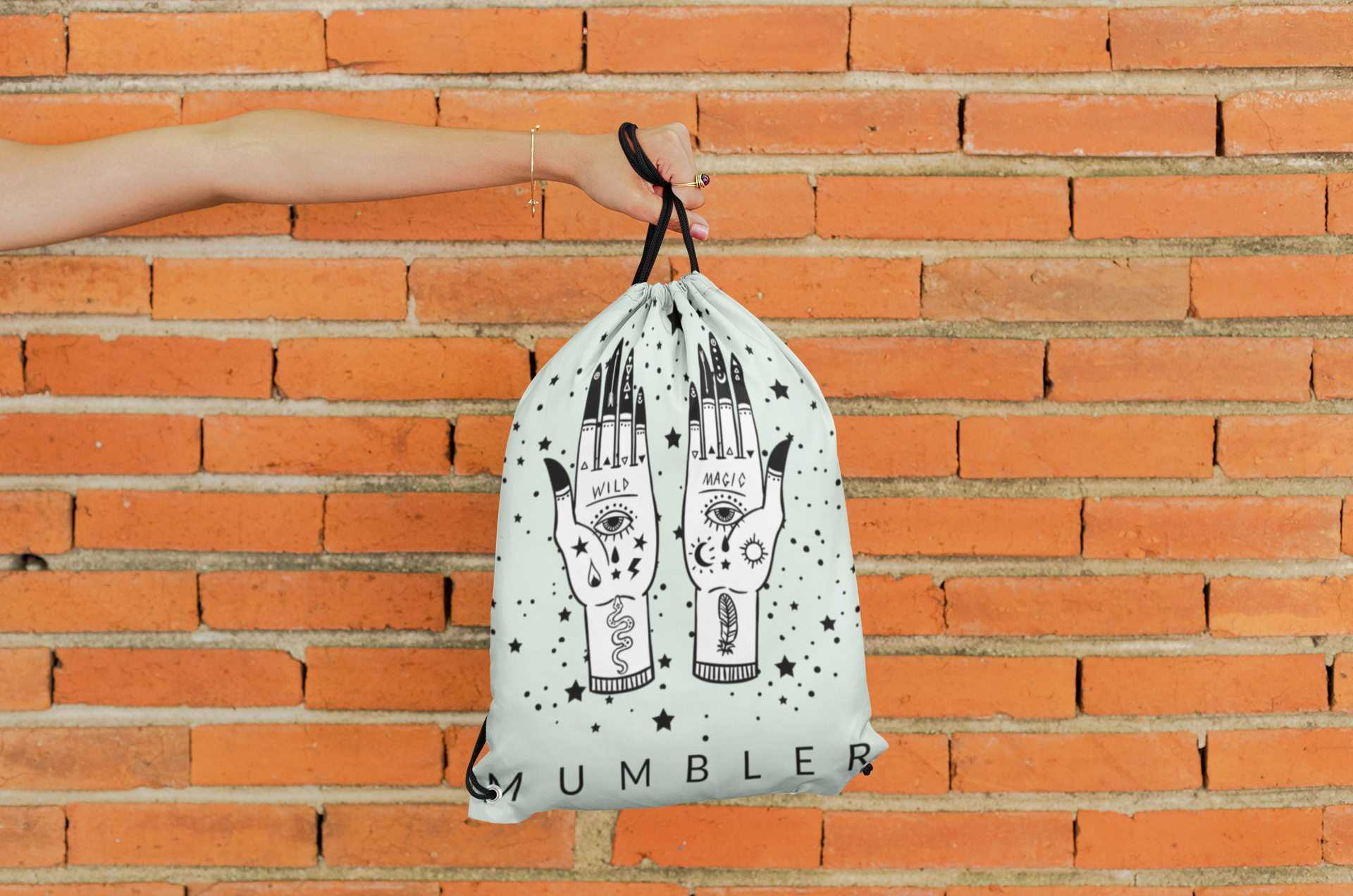 mockup-of-a-hand-holding-a-drawstring-bag-against-a-brick-wall-27574.png