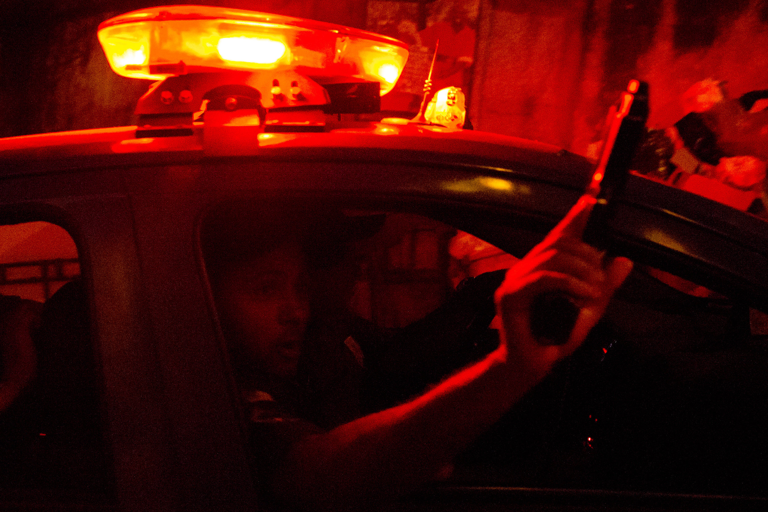  A Rio de Janeiro military police officer waves his gun out of the car while driving down the street after a protest in which police intervened. (Courtney Pedroza/Cronkite News)  &nbsp; 