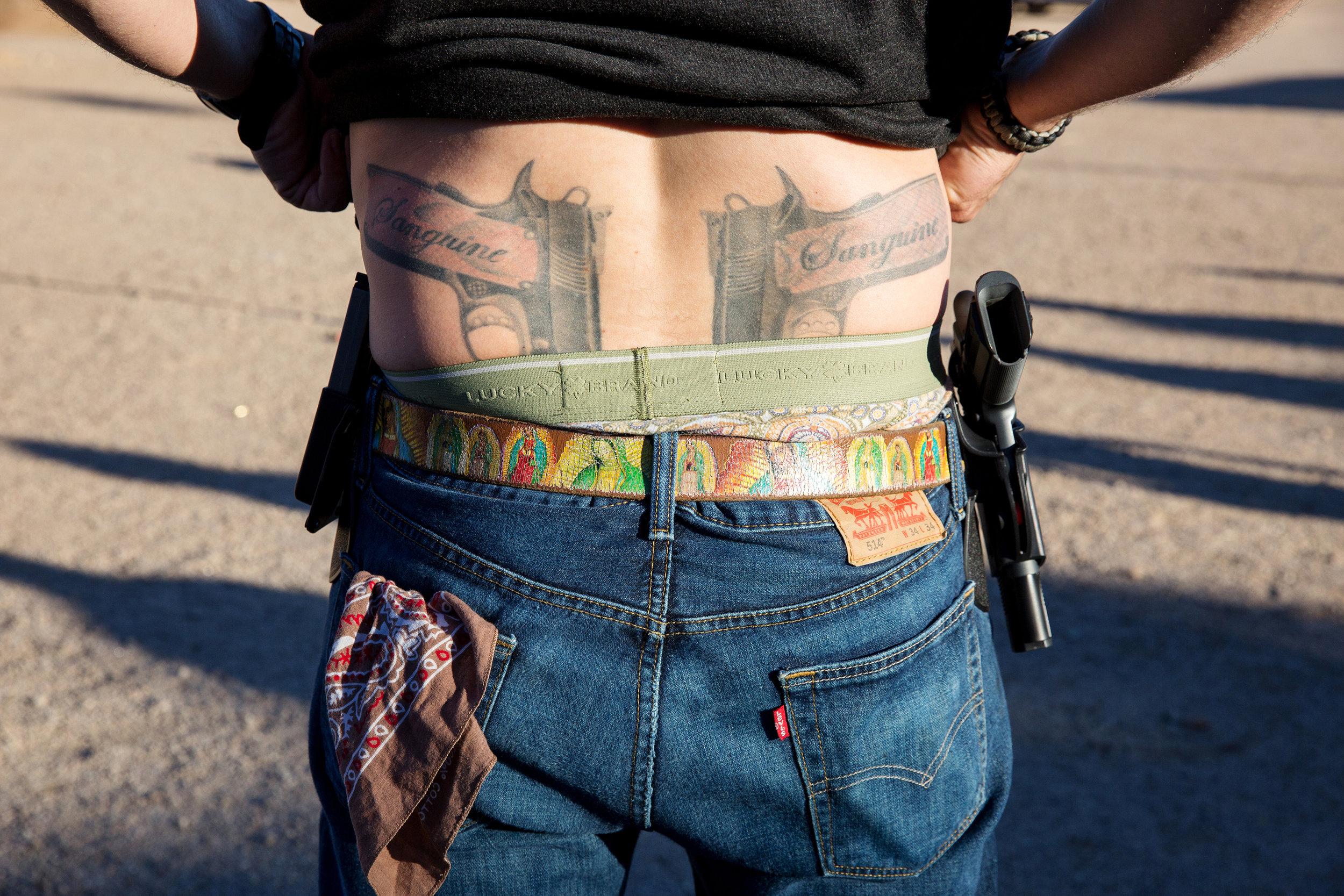 Joe Proctor lifts up his shirt to show his tattoos of guns that read “Sanguine” on the grips at the Rio Salado Sportsman’s Club on Jan. 30, 2016, in Mesa, Arizona. His worn-down belt features the Virgin Mary, and he carries an unloaded gun on one hi