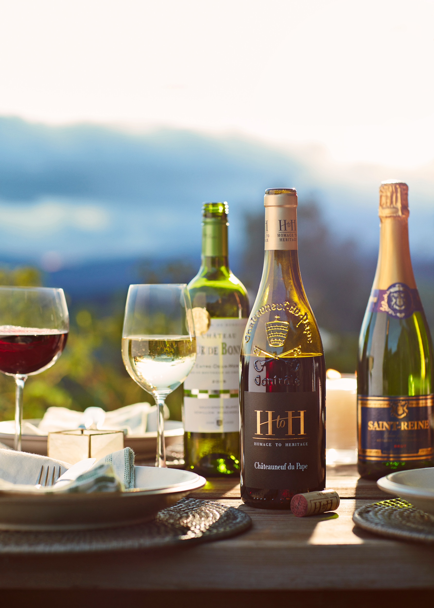 A selection of red and white wine bottles on a tabletop outdoors. Wine tasting and place settings.