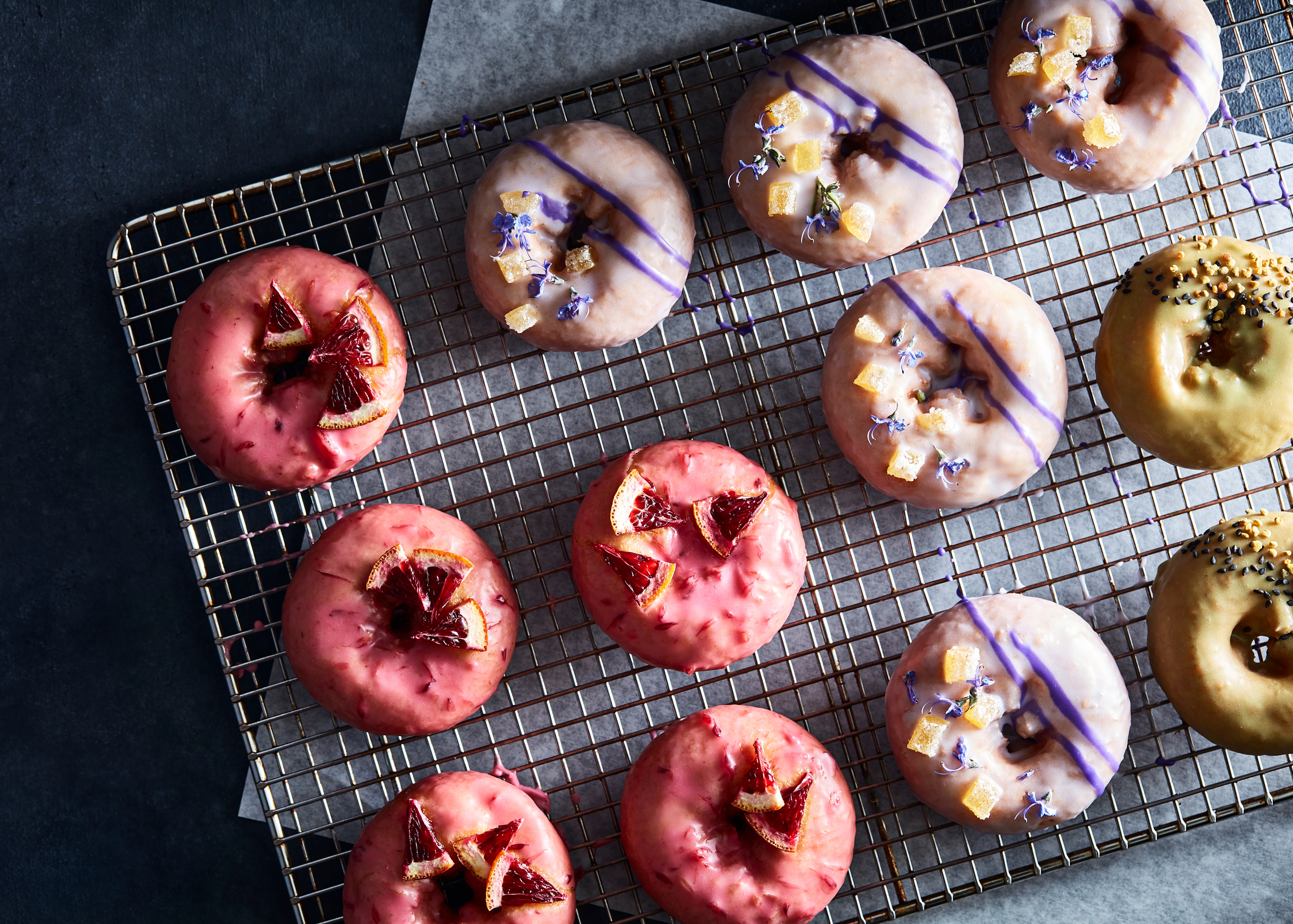 Assorted colorful cake donuts on cooling rack with parchment underneath.