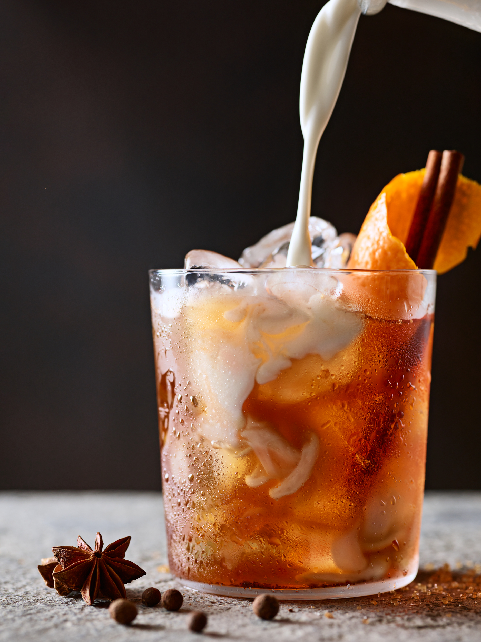 Chai latte with cream pour with a cinnamon stick and orange twist.