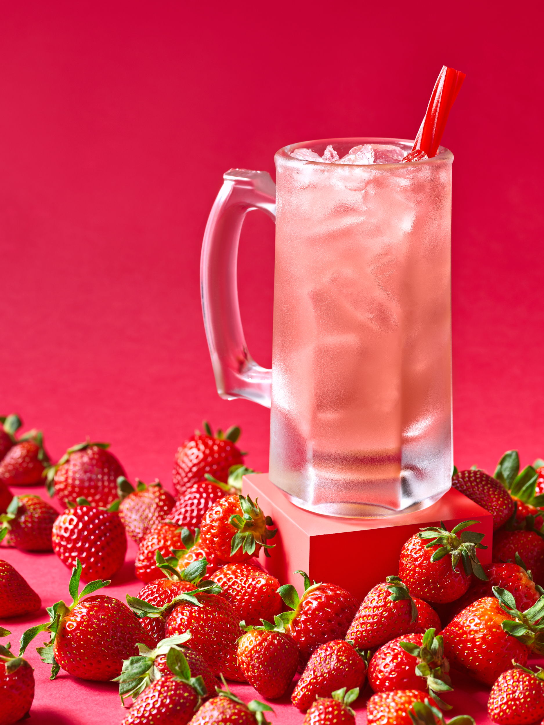 Strawberry cocktail on a pedestal amidst a sea of ripe red strawberries.