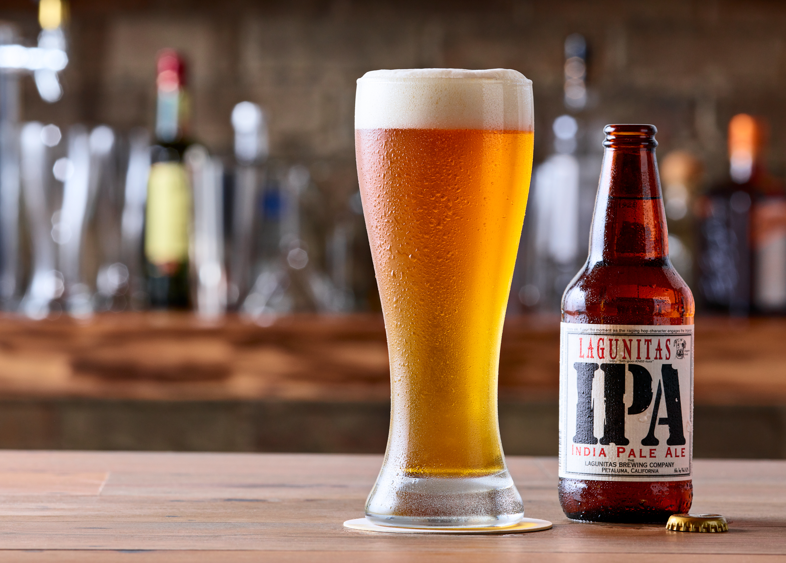 Lagunitas IPA in a pint glass and bottle on a bar top.