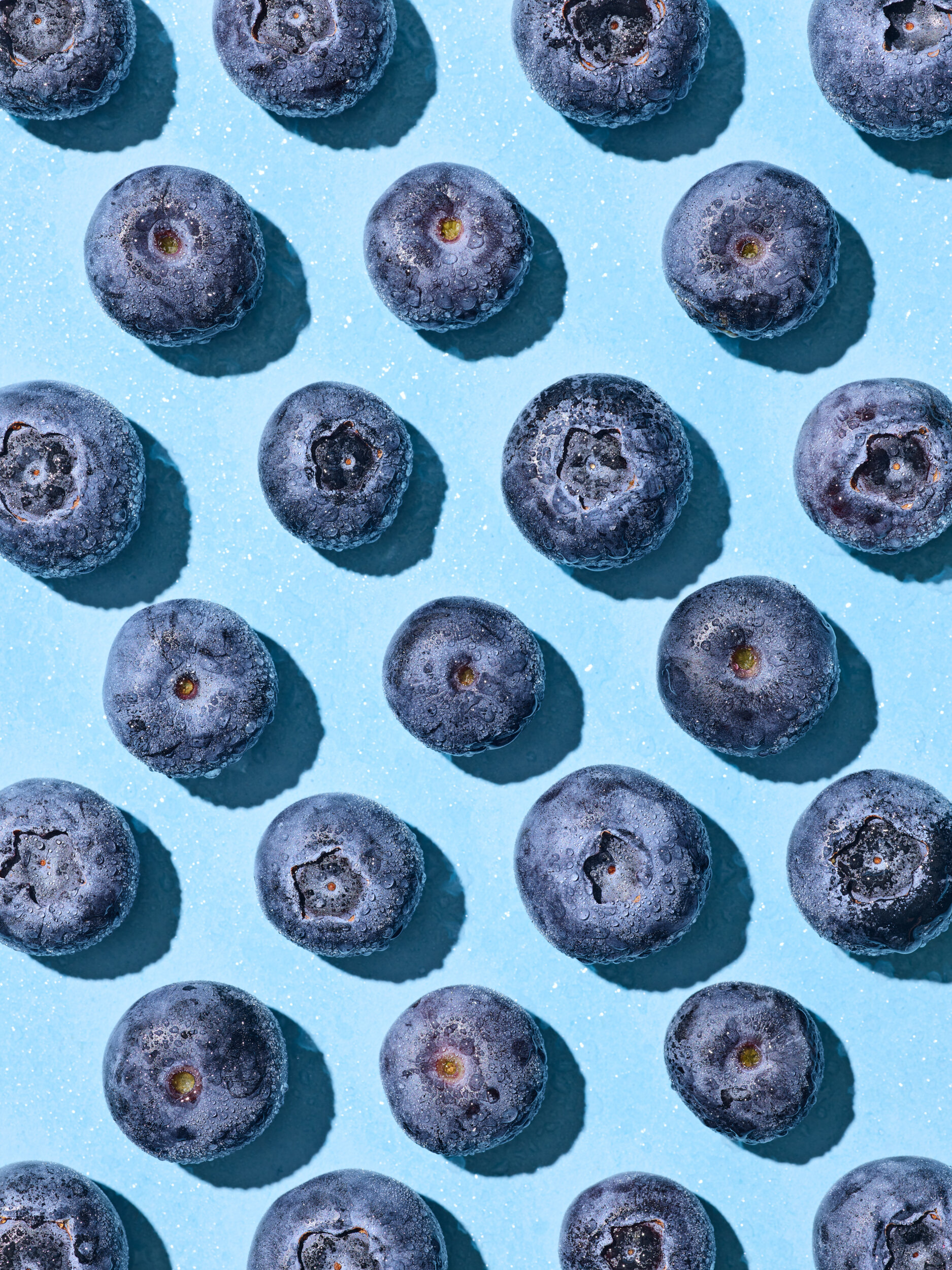 Overhead image of blueberries in a graphic composition on a blue backdrop.