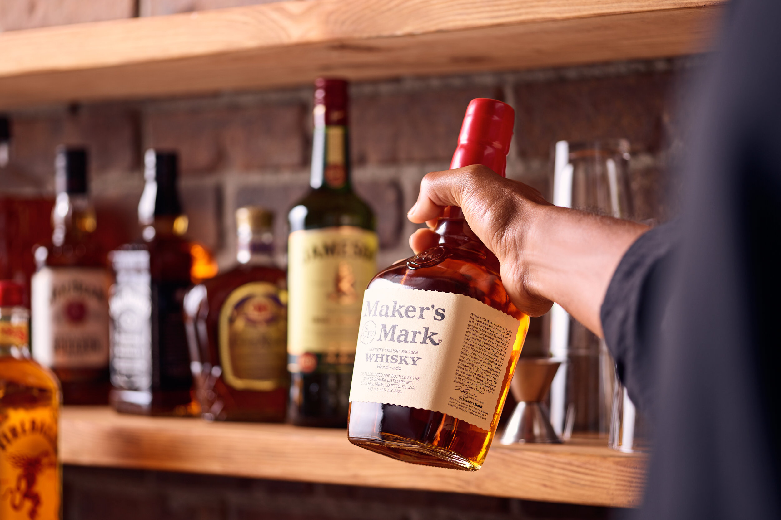 Bartender pulling a bottle of whisky off of a shelf filled with spirits.