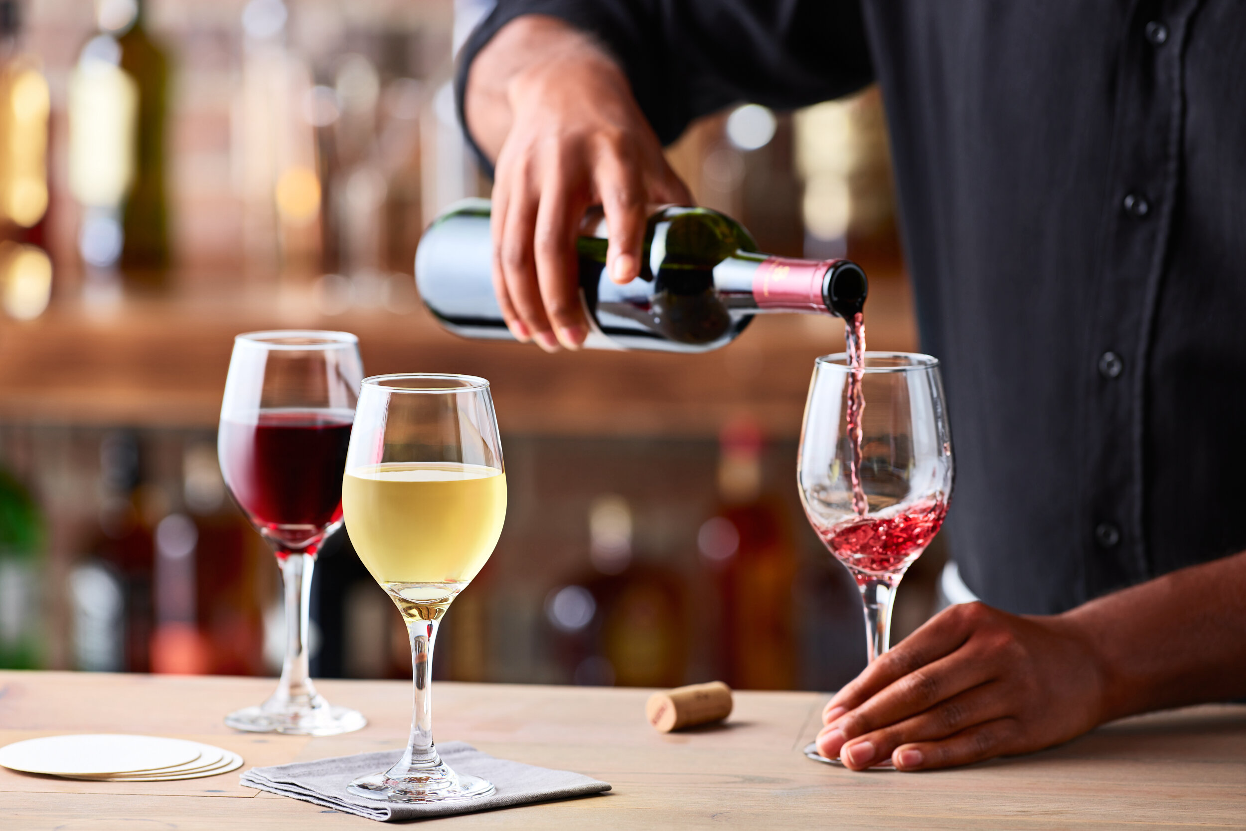 A bartender in black shirt pouring wine in a mostly wooden bar setting.