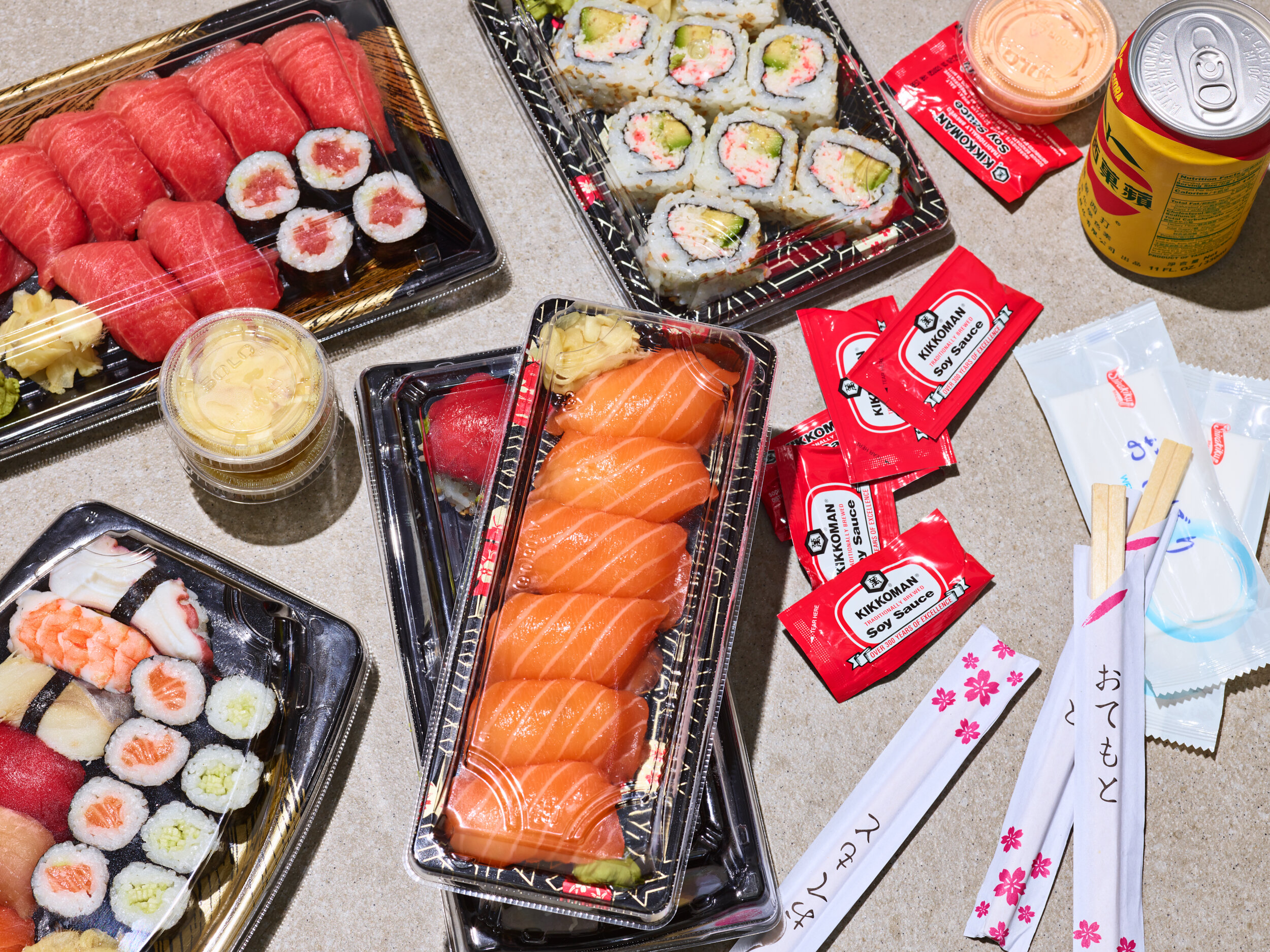 Sushi delivery from a Los Angeles restaurant in plastic packaging with serving utensils and a can of soda. Salmon, tuna, california roll, sashimi, toro, unagi, tomago. 