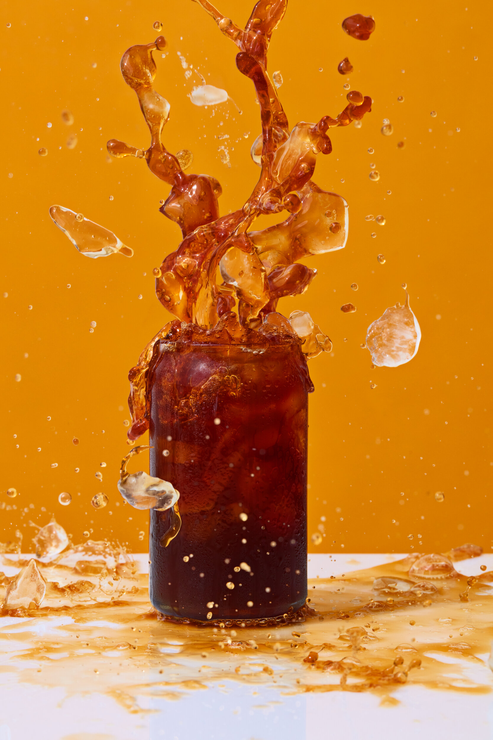 Iced coffee splash photography. Yellow backdrop and white surface.