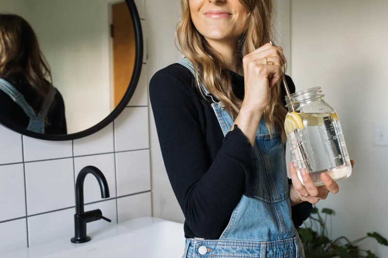 Blogger sits by counter top and drinks her water. Emily recommends 8-10 glasses of water a day.