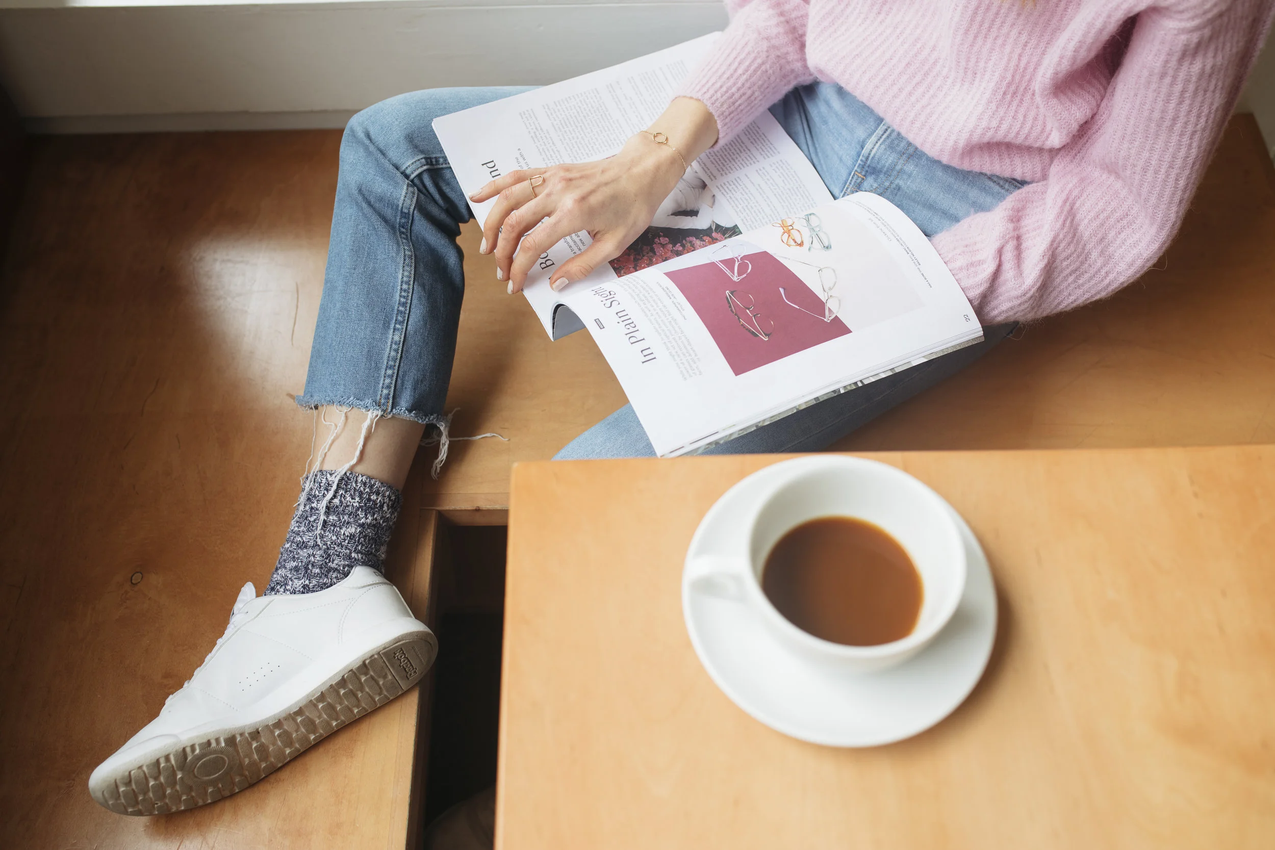 Studying fashion and drinking coffee in a pink ethically made Everlane sweater