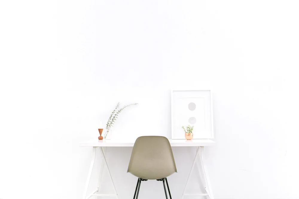 A minimalist home office desk with a chair, plant, and picture frame
