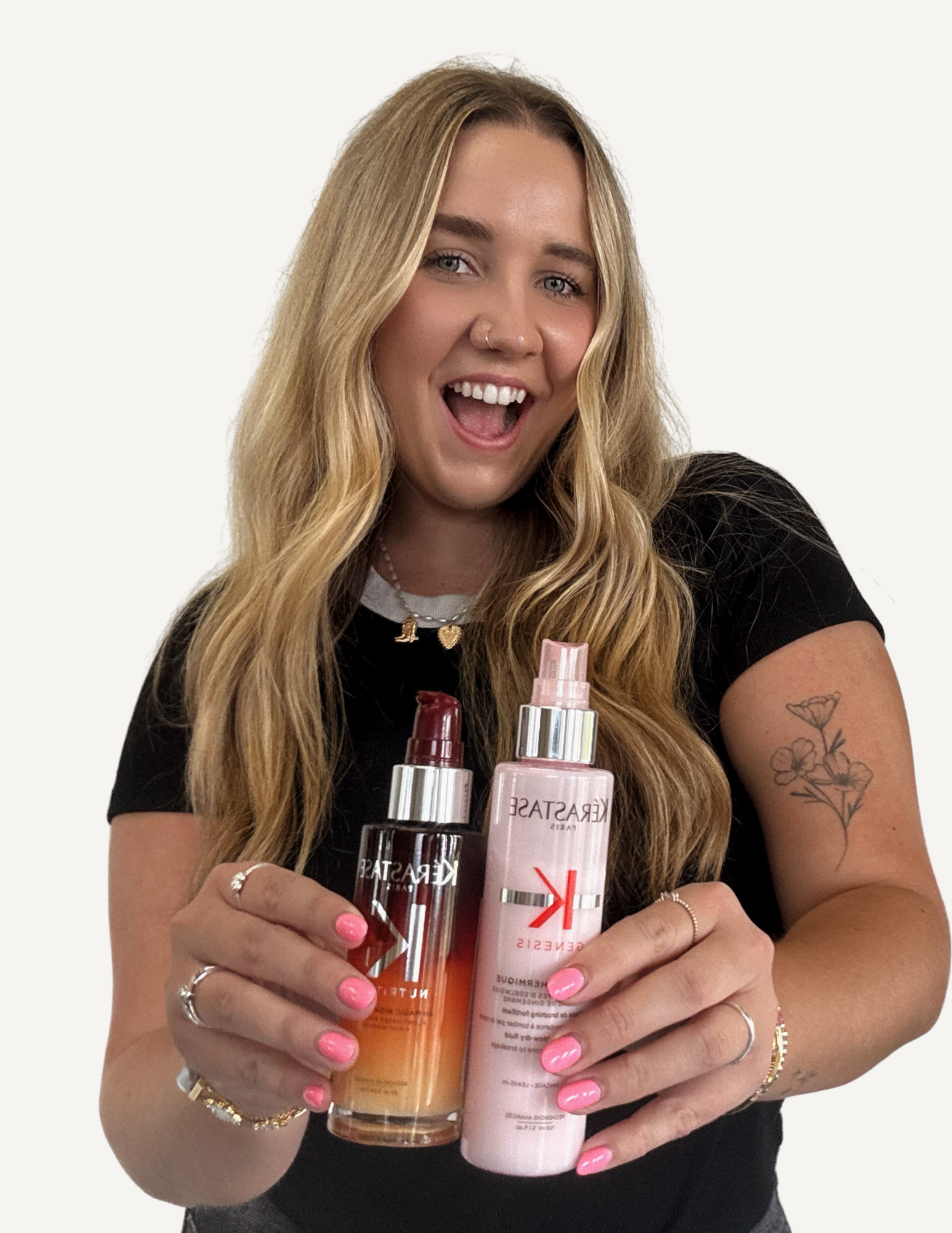 A woman with long, wavy red hair, smiling, wearing a black short-sleeved shirt and a delicate necklace, sitting indoors against a plain white wall.