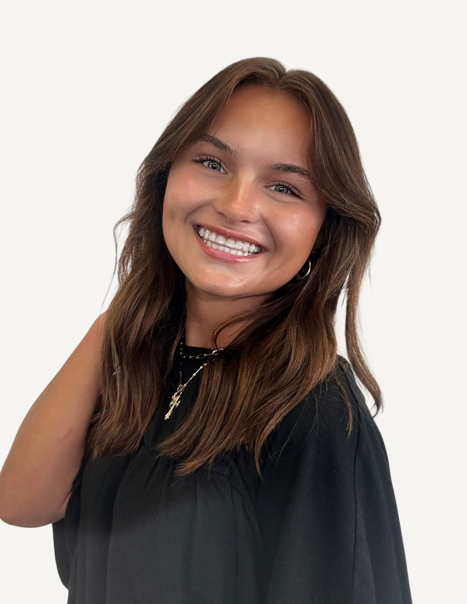 A young woman with wavy brown hair, blue eyes, and pink lipstick, smiling in a modern, brightly lit indoor space.