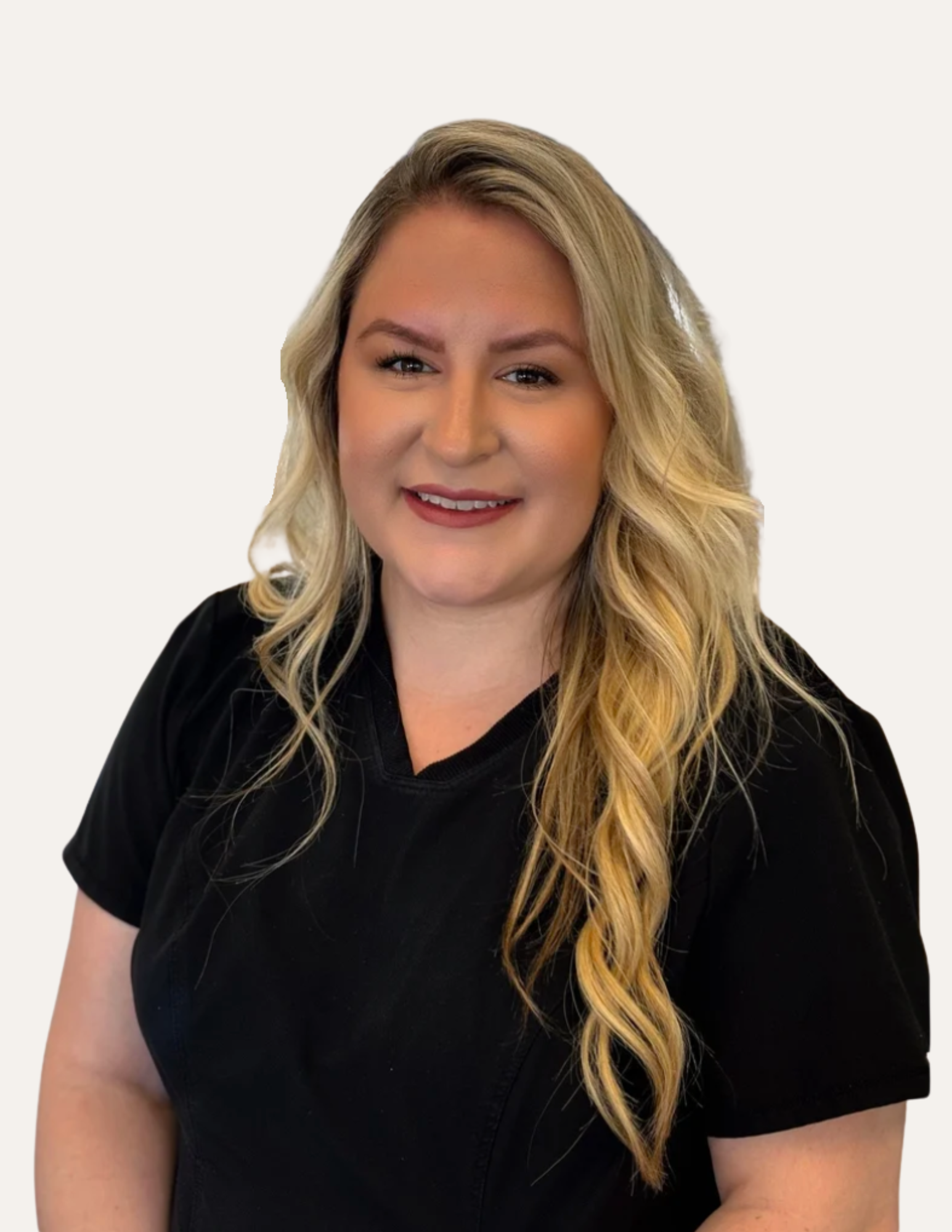 A smiling woman with long wavy blonde hair wearing a black shirt, standing inside a store with shelves stocked with personal care and beauty products.
