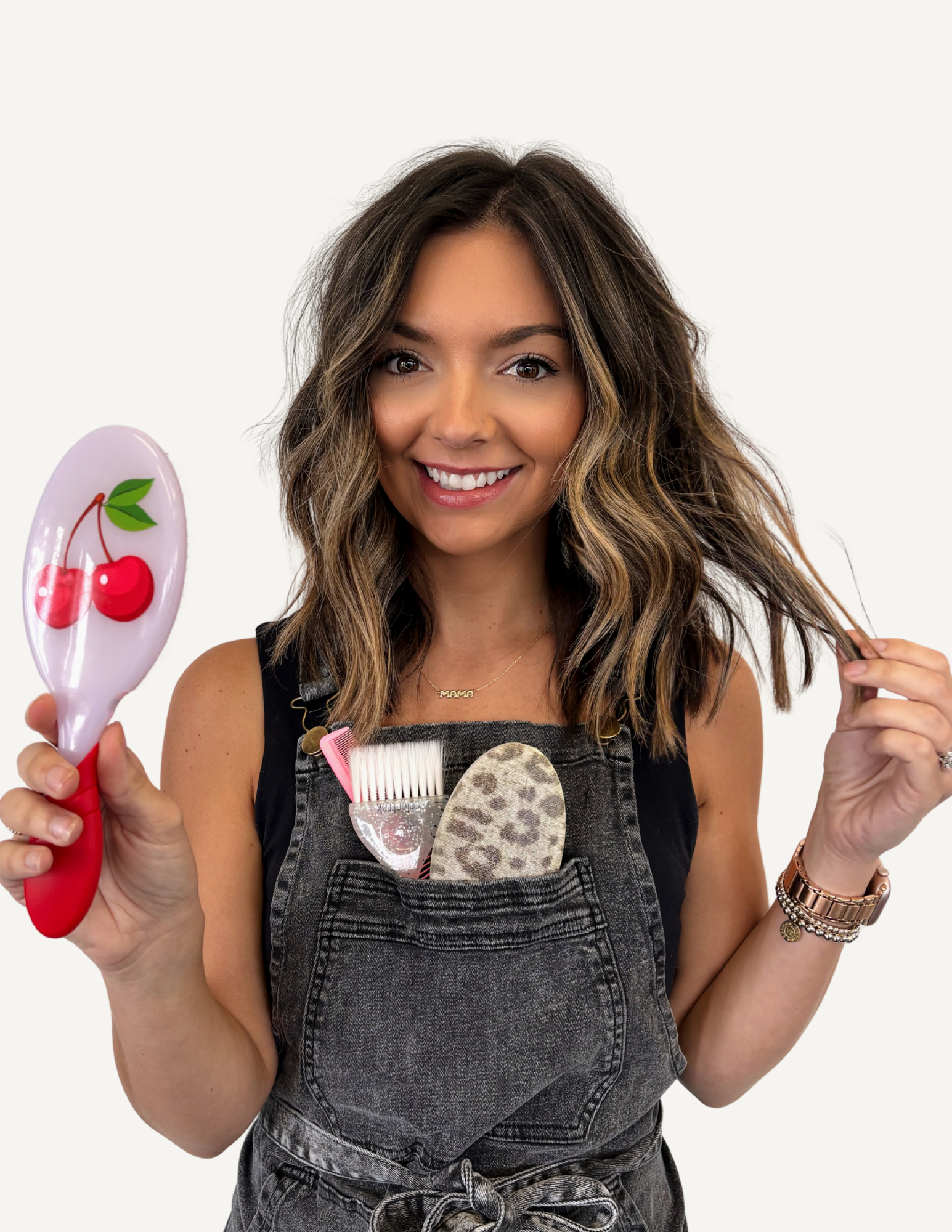 A smiling woman with long wavy blonde hair, wearing a black sleeveless top and a smartwatch, sitting in a salon or similar setting.