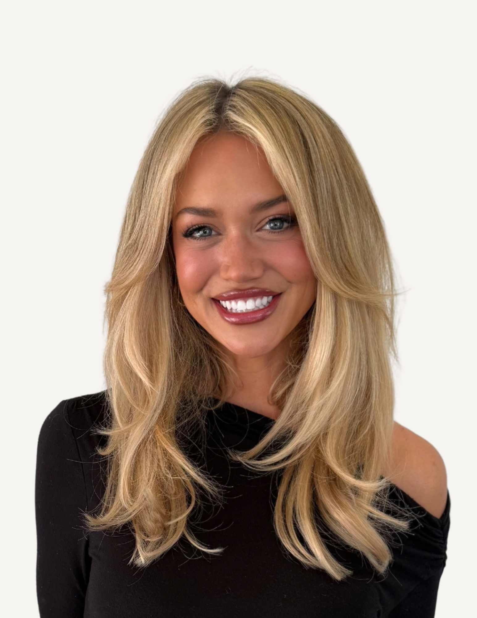 A smiling woman with blonde hair wearing a black lace-trimmed top and layered gold necklaces in an indoor setting.