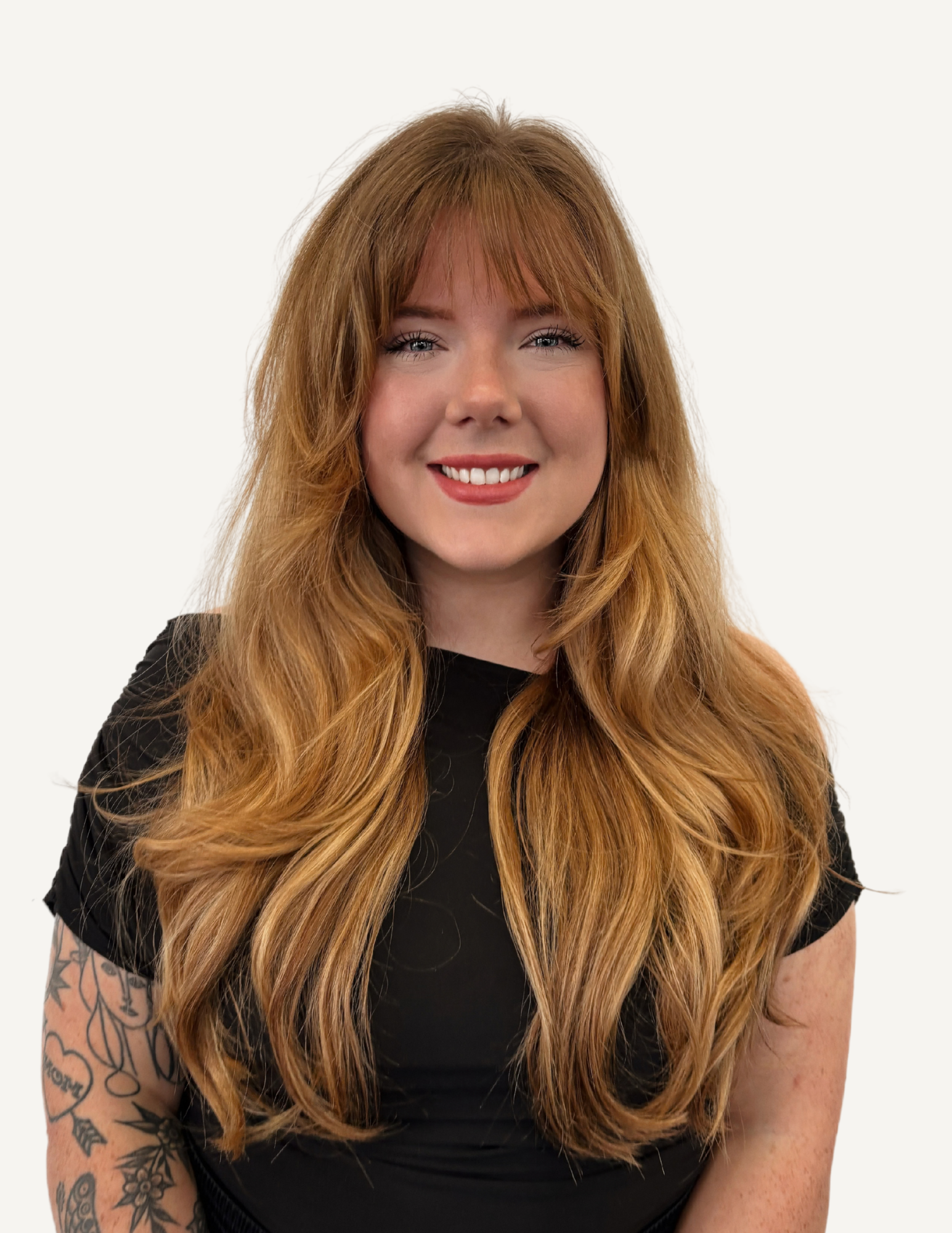 Portrait of a smiling woman with long red hair and blue eyes, wearing a black off-shoulder top, in a well-lit indoor setting.