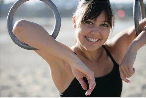 Smiling woman exercising outdoors with gymnastic rings at the beach.