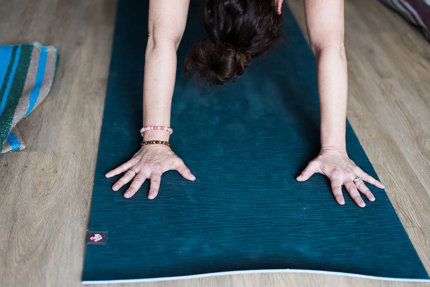 Person performing yoga downward dog pose on a black yoga mat on a wooden floor.
