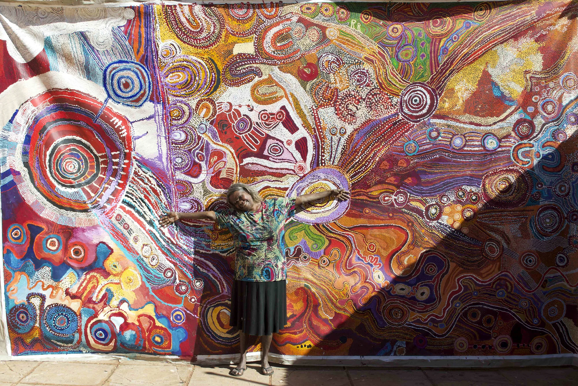 Artist Nyukana Norris standing with the WOMEN'S collaborative painting at Kaltjiti (Fregon), 2016. Image courtesy Kaltjiti Arts, Fregon.