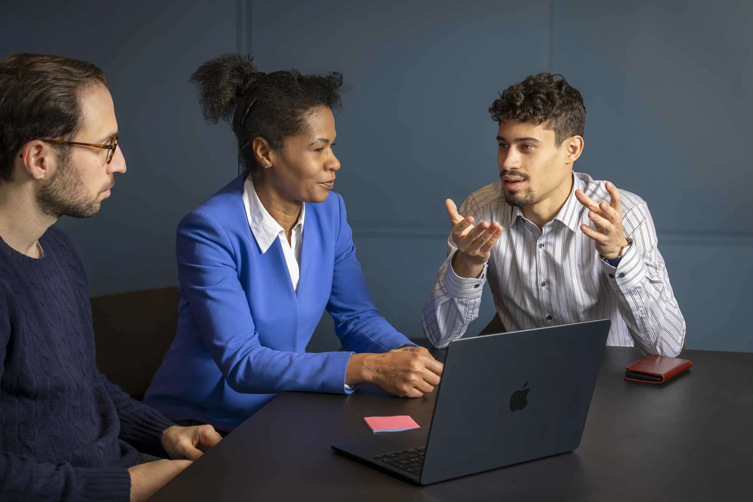 Drei Business-Leute in Diskussion an Tisch in edlem Sitzungszimmer