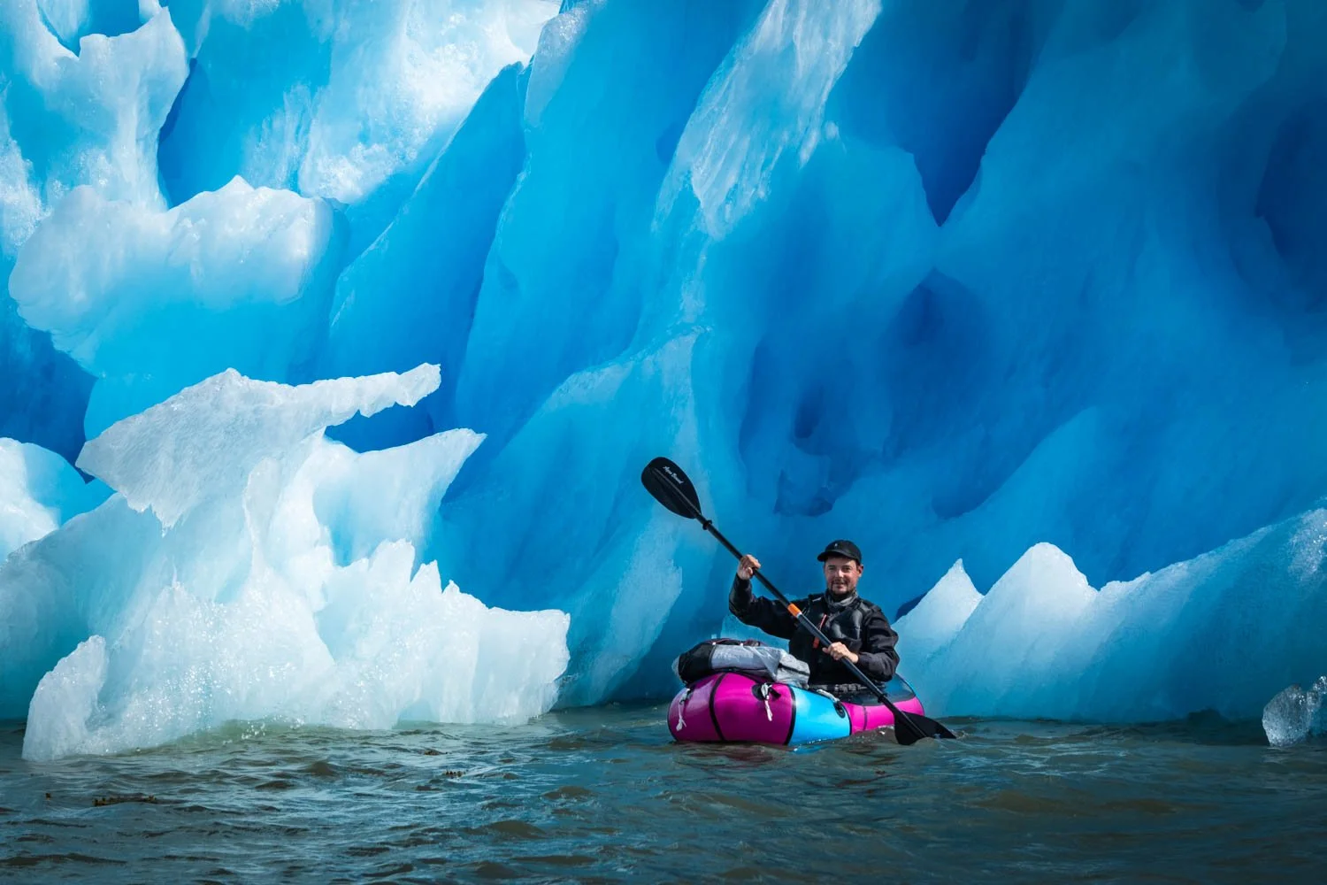 Josch mit Packraft vor riesigem blauem Eisberg in Grönland