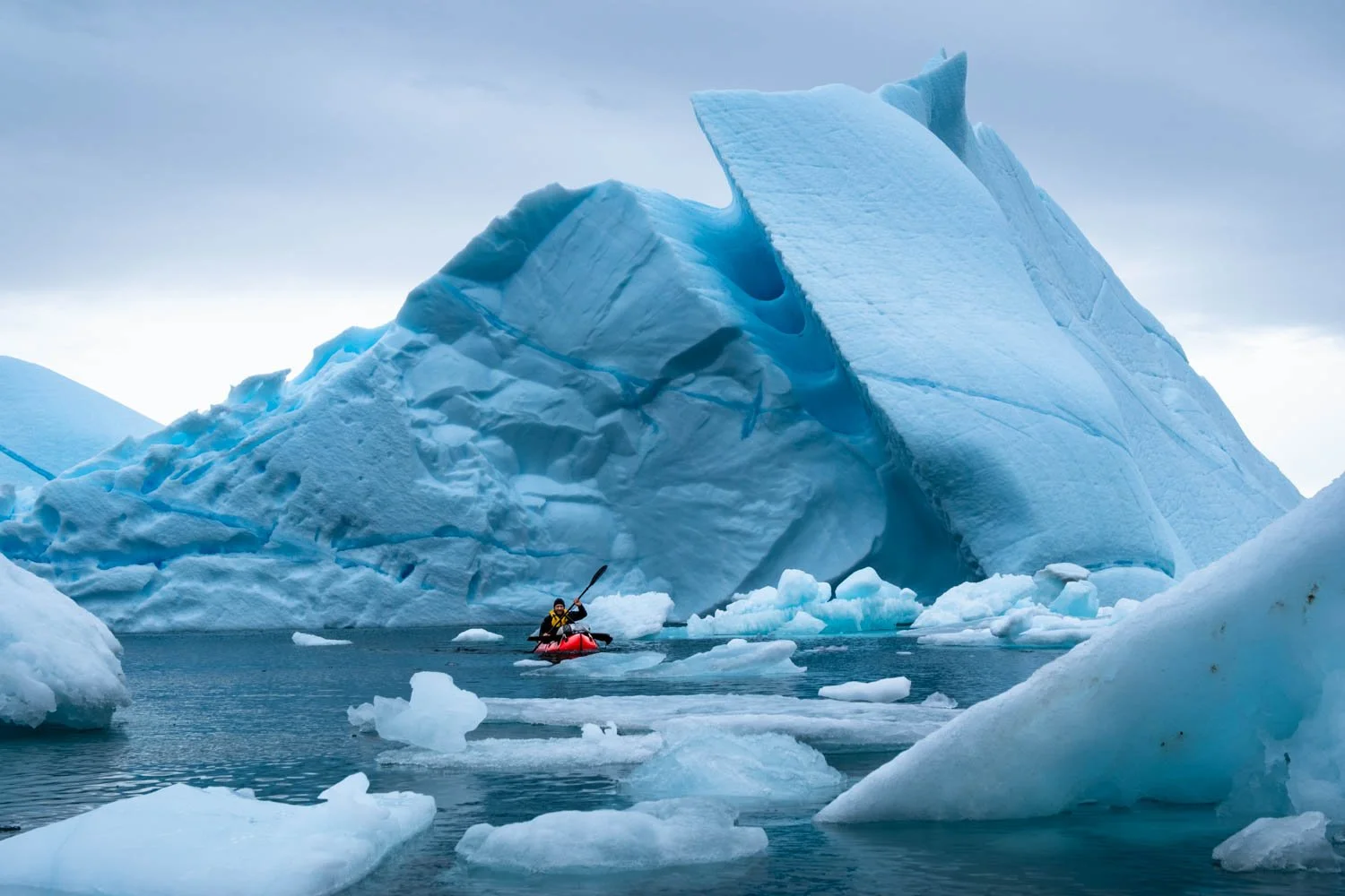 Fotograf Martin Ramsauer mit seinem leuchtenden Packraft inmitten von Eisbergen in Ostgrönland