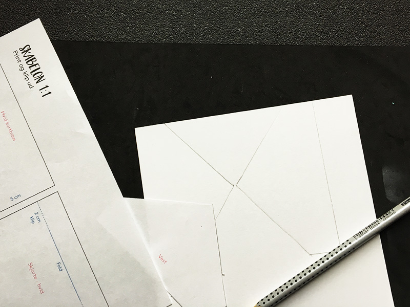 Step 6: Skær vesten i dit valgte designpapir. Brug skabelonen eller mål selv ud. Her har jeg brugt skabelonen og tegnet den bag på mit papir. Derefter har jeg brugt min skæreplade til at skære efter stregerne. Jeg har brugt Three Scoops designpapir med sorte v’er. Papiret kan du finde i shoppen her .