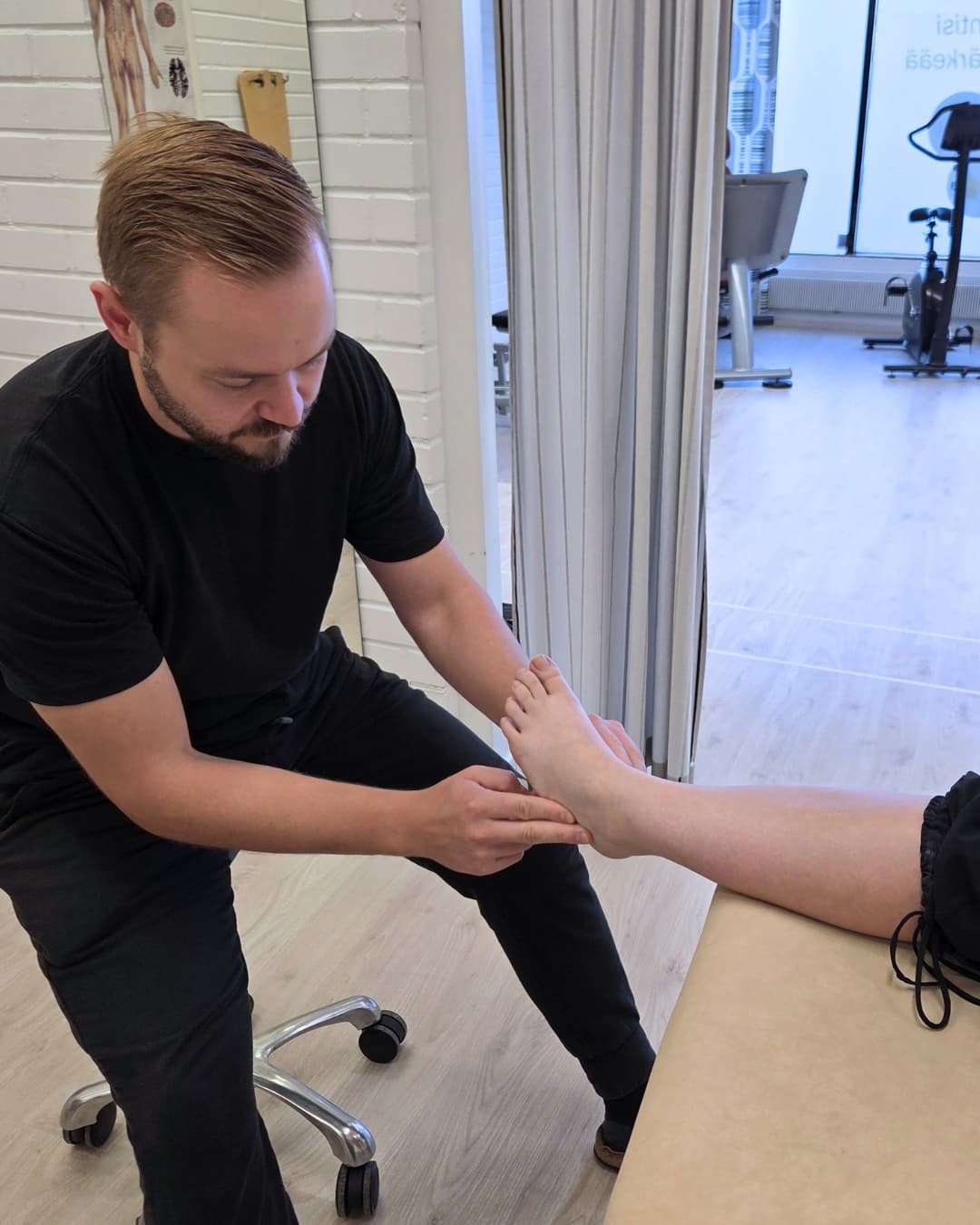 Fsyioterapeutti tutkii asiakkaan nilkkaa.