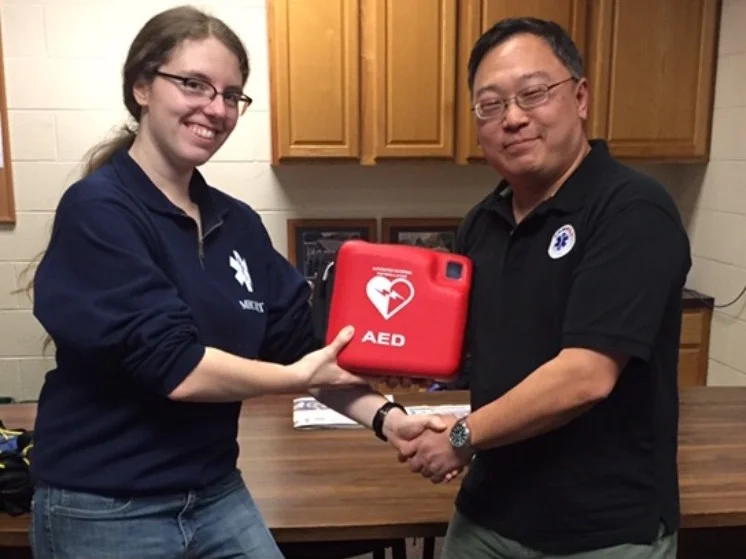 Photo courtesy of MERT Director of MERT, Louise Tanner ’19, accepts a new AED from Dr. Tae Kim, a local medical director.