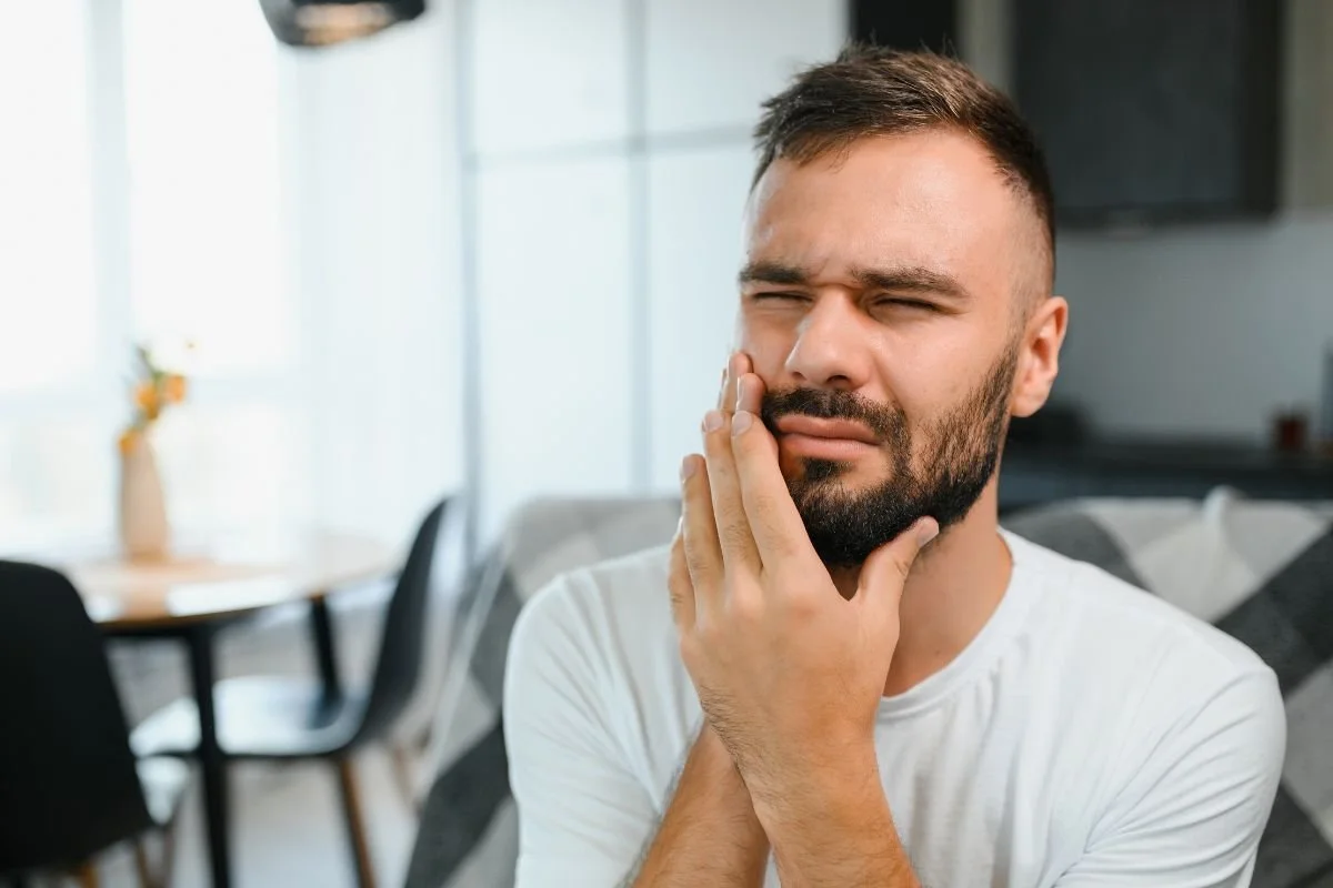 Man with beard holding mouth to express toothache pain