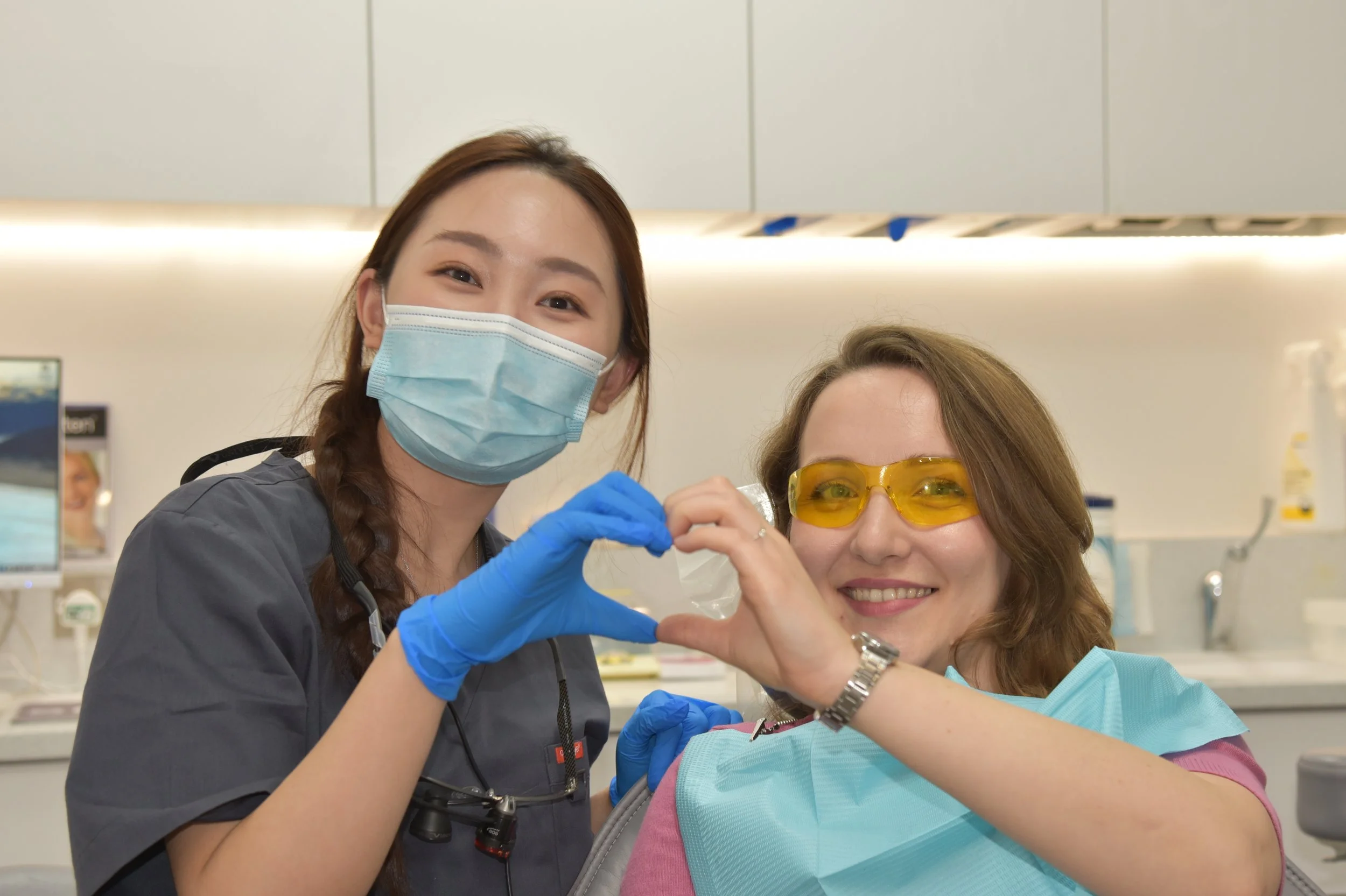 Mandarin speaking Dentist with patient making heart shape with hands, whilst in dental chair