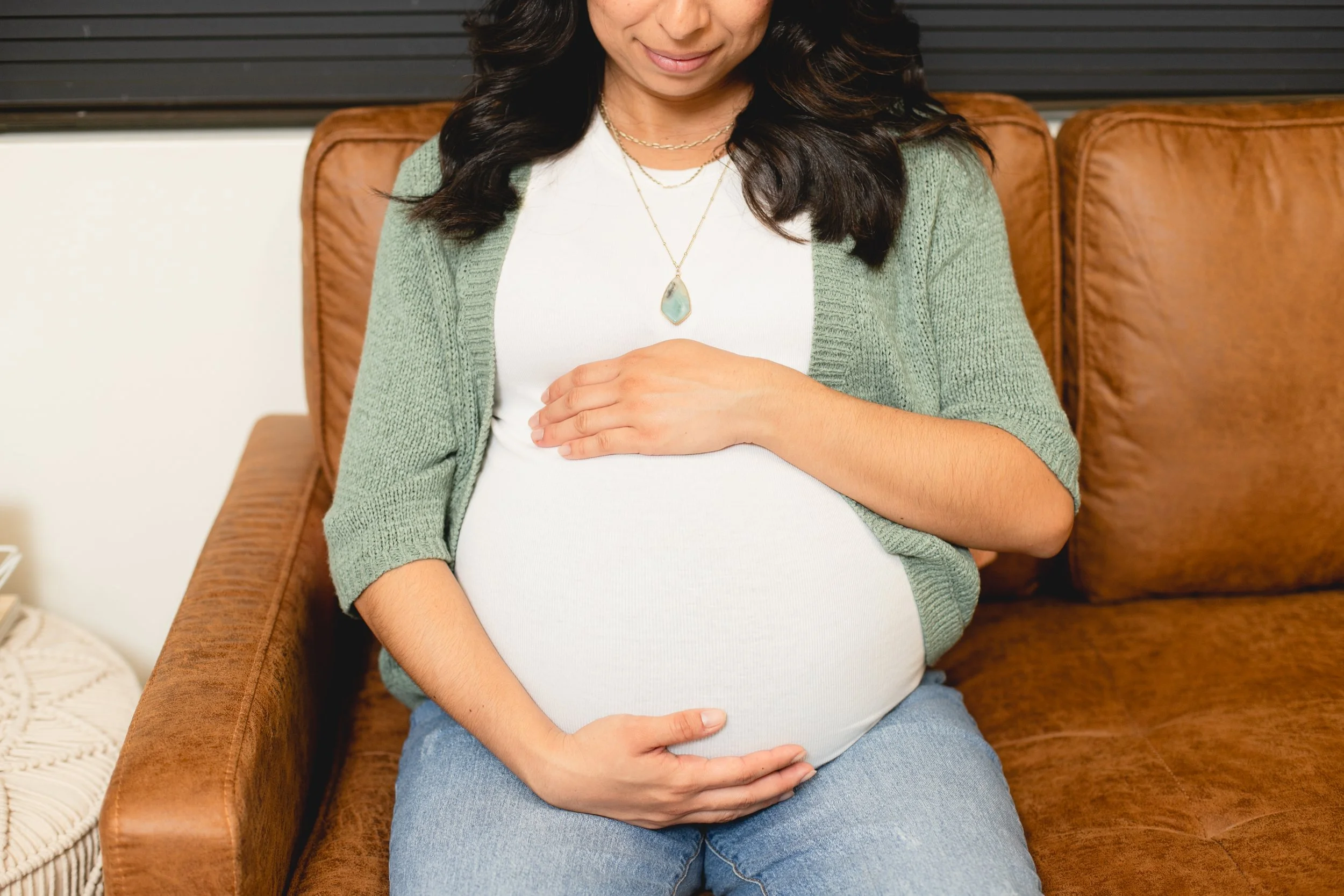 A pregnant woman holding belly while sitting in on breastfeeding class in San Diego, California.