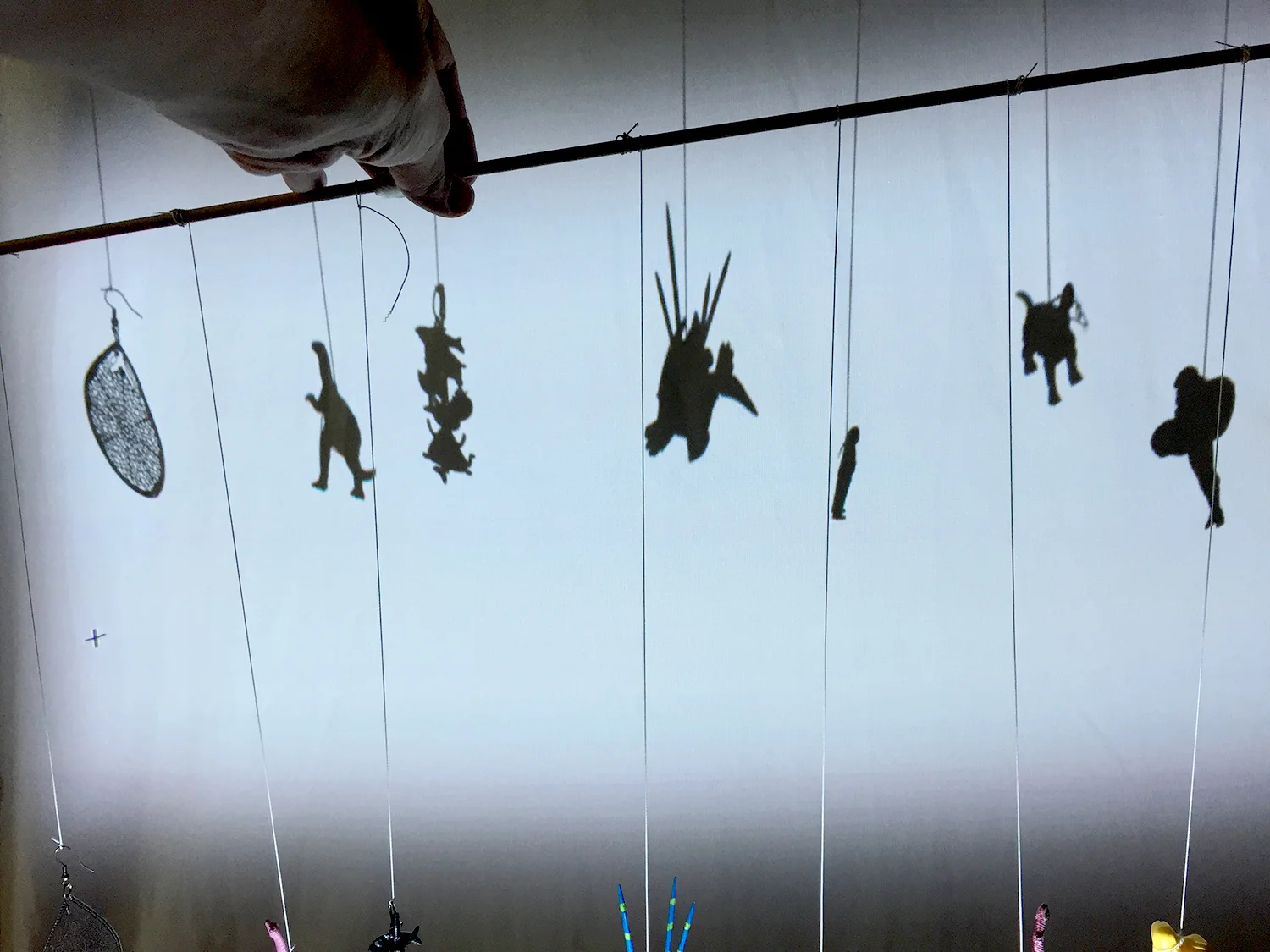 Shadow of "Little people" Found objects: Earrings, little dinosaurs, miniature human figure Wooden dowel, string
