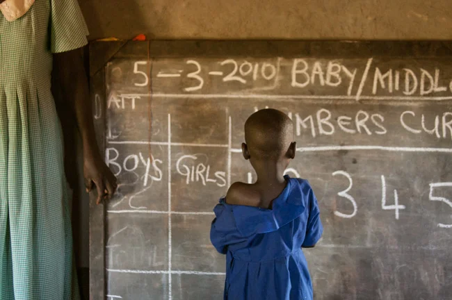 The day in the life of a Ugandan teacher begins before dawn. She rises early to collect firewood, feed her children, and clean her home. She takes pride in being professional and spends a little time getting ready for her job. Then she walks several miles to her school. She teaches forty six year olds in a one-room mud building and holds the future of Uganda in her hands. Obaya Community Association provides teacher training to rural communities and in return the teachers help fund other teachers once they receive a salary. It is a grassroots operation that helps the community raise education standards from the inside out. Photo courtesy of © Crystaline Randazzo