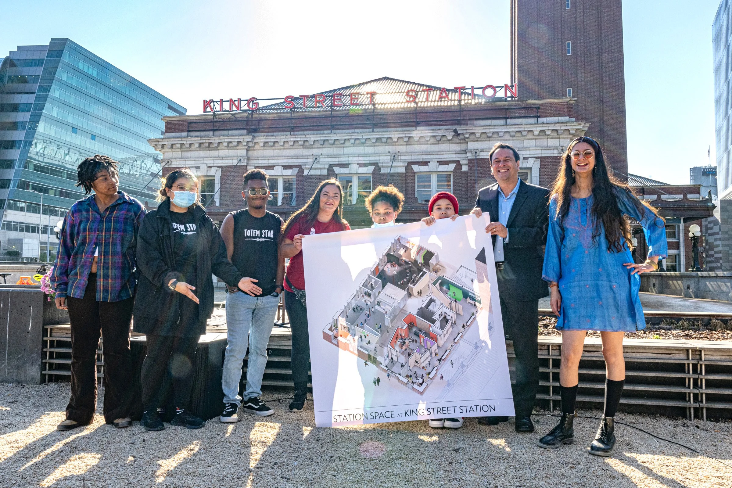 Youth representatives from Totem Star and Rhapsody Project stand with Deputy Mayor Greg Wong, holding a rendering of the new Station Space project at King Street Station. Photo by Photo Bakery.