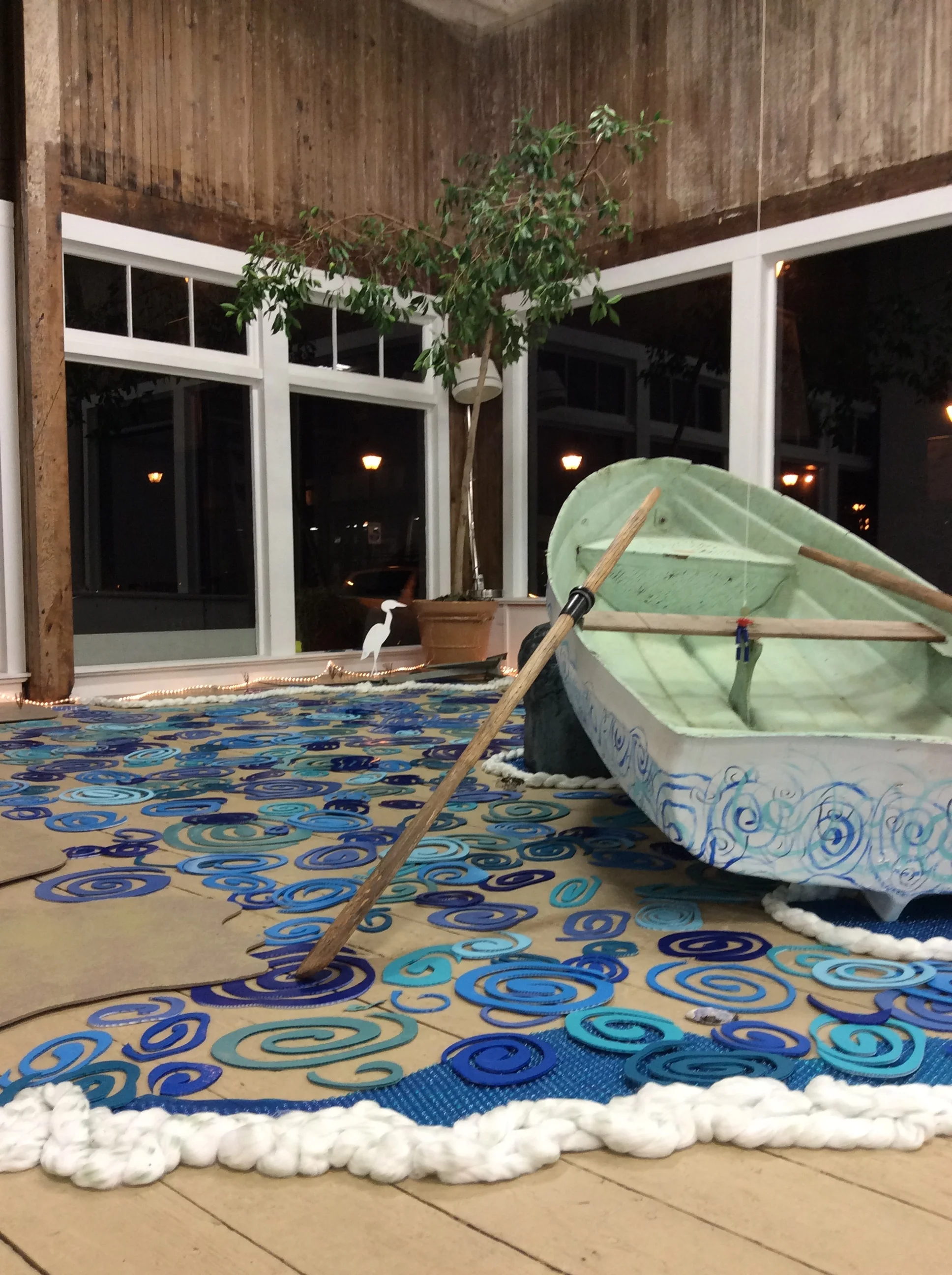 Aquatic inclinations of the disaster prone. - Installation with boat, repurposed campaign signs, Styrofoam blocks, cotton rope, floor runner, reclaimed wooden oars –altered & stained, paint, wood, string, pulleys, handle, reclaimed USCG anchor, twist ties, wax, varnish, string, caulk, sea shells, barnacles. 2019