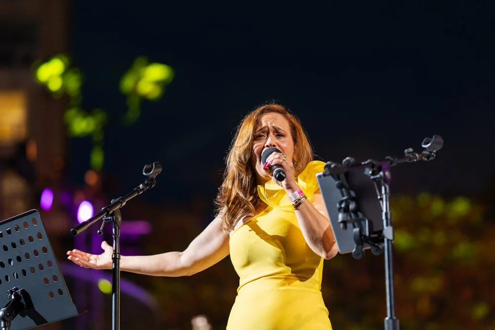 Iris Sandra Cepeda singing on stage in a yellow dress at Grand Performances