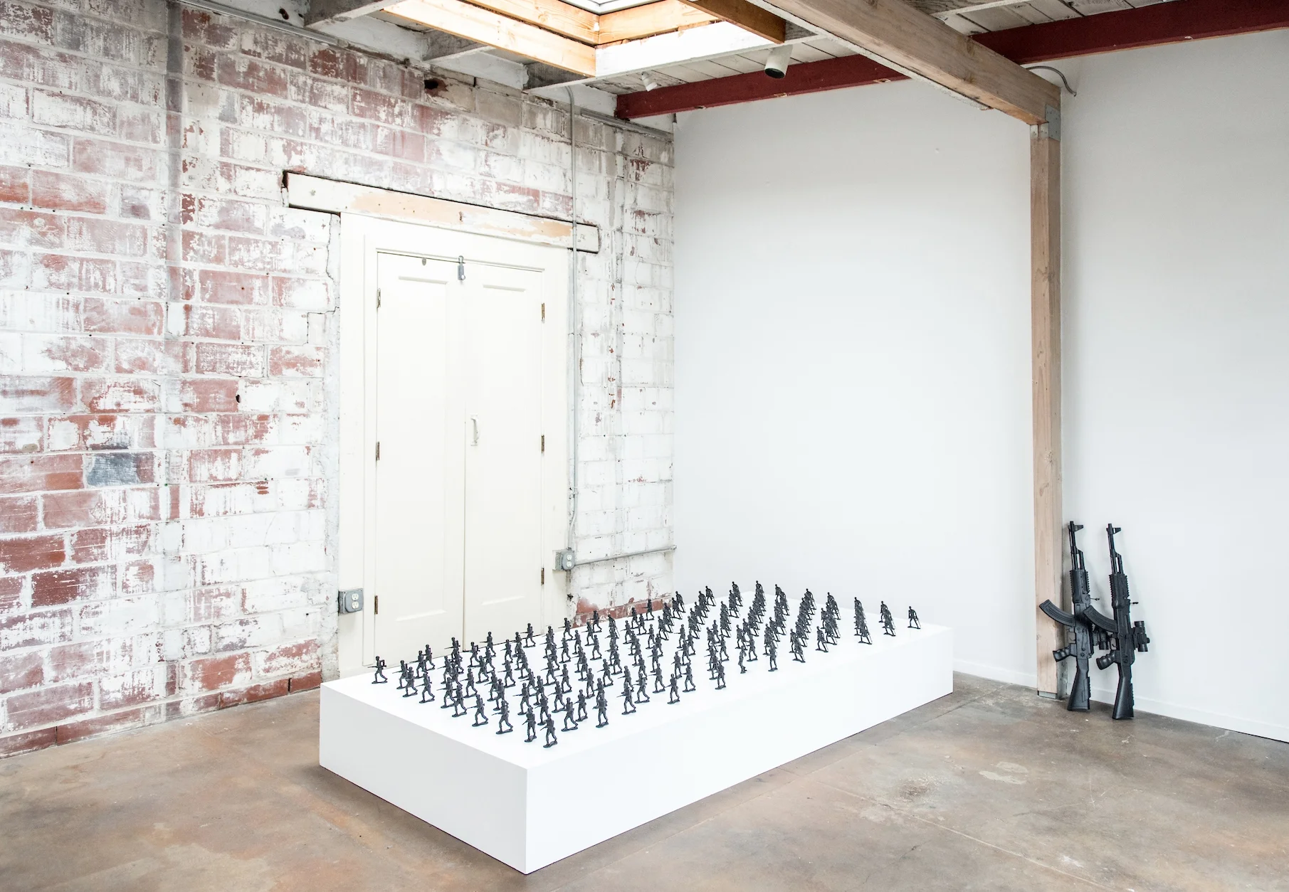 Installation View.Wooden platform, toy soldiers (4”), toy AK-47 assault rifle (2½ ft), aerosol paint.
