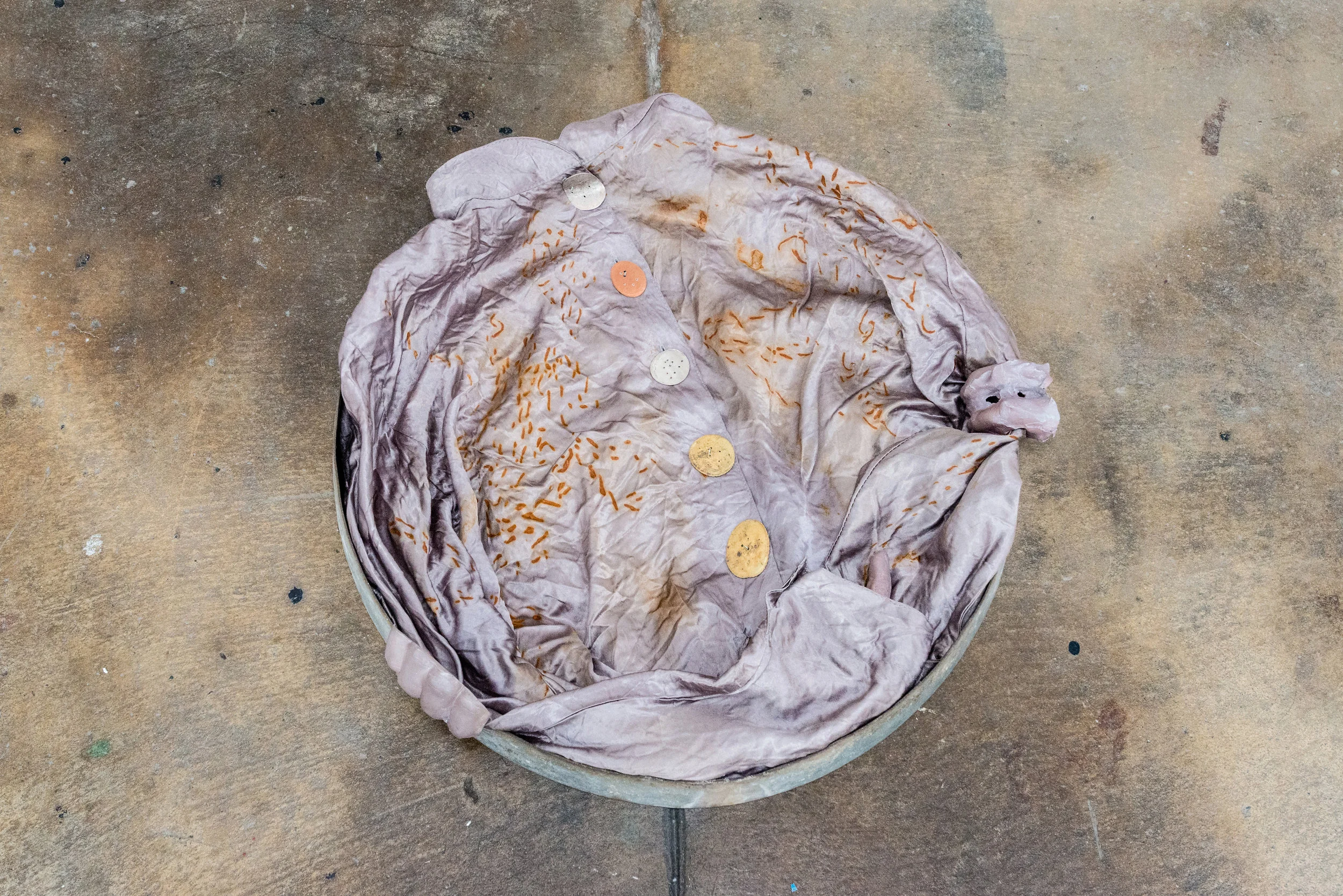 Jenine Marsh, contortion (silver) , 2018. Found metal ring, rust-stained blouse, train-flattened and drilled coins of mixed currencies, wire, gypsum cement, powdered pigment.