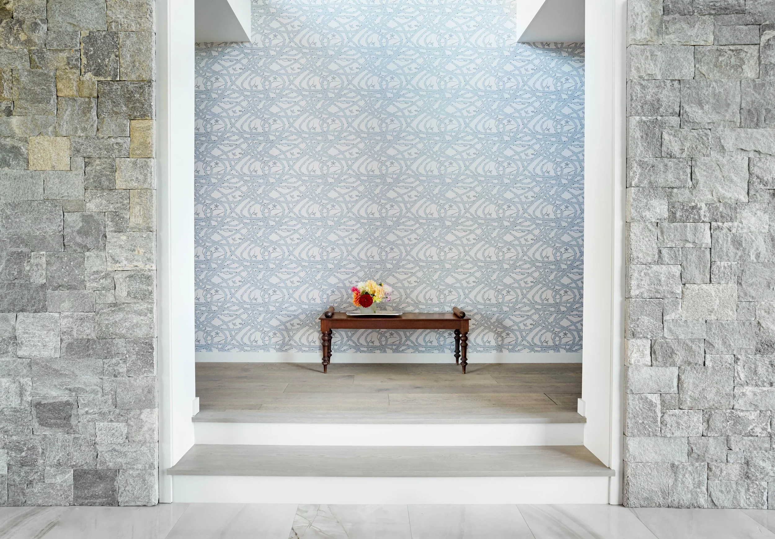 Bramble Wallpaper by Abigail Edwards in a grand yet modern hallway with steps framed by  an elegant grey stone wall