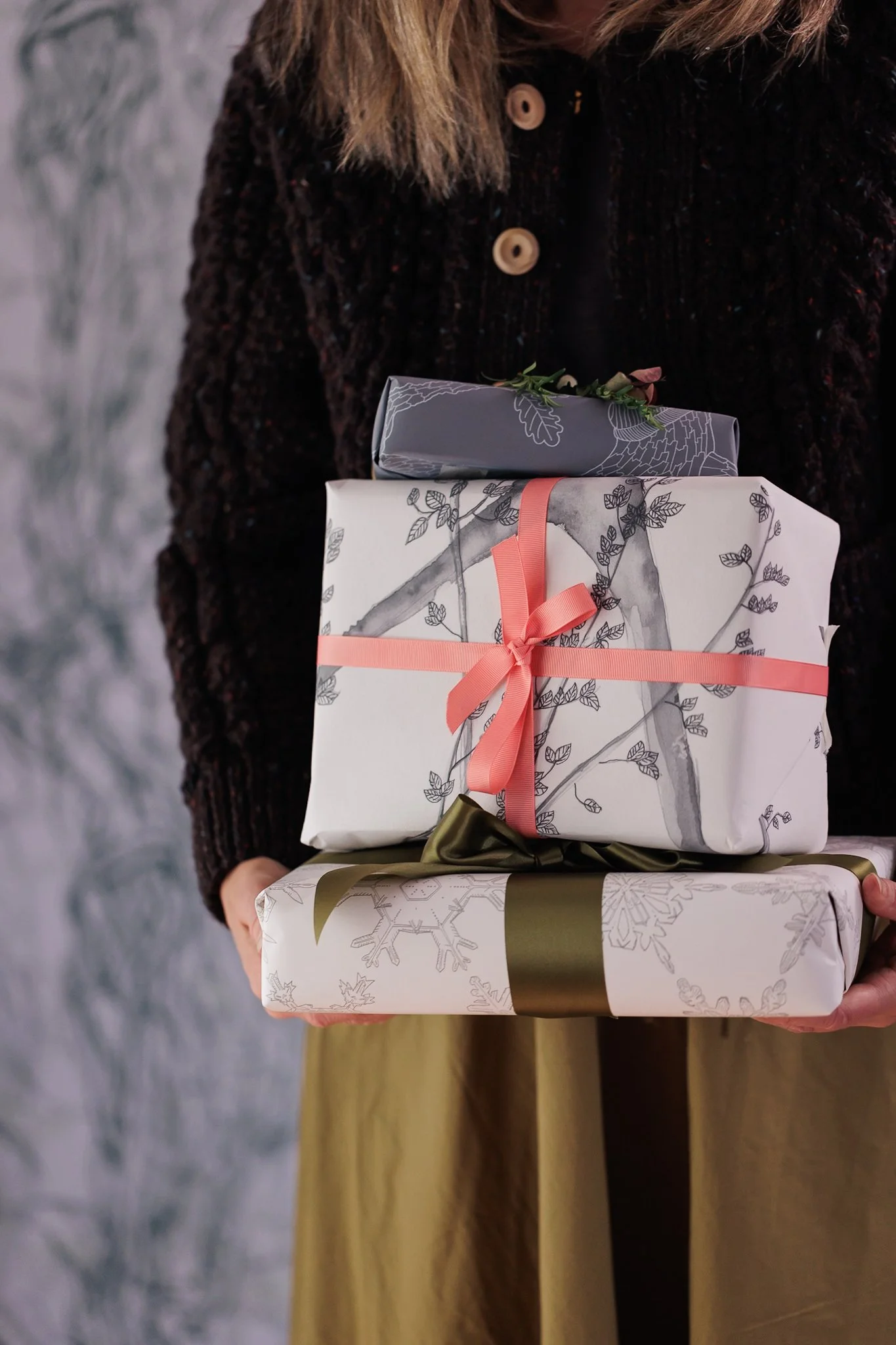 A woman holding a pile of Christmas presents wrapped in wallpaper offcuts by Abigail Edwards tied with satin ribbon