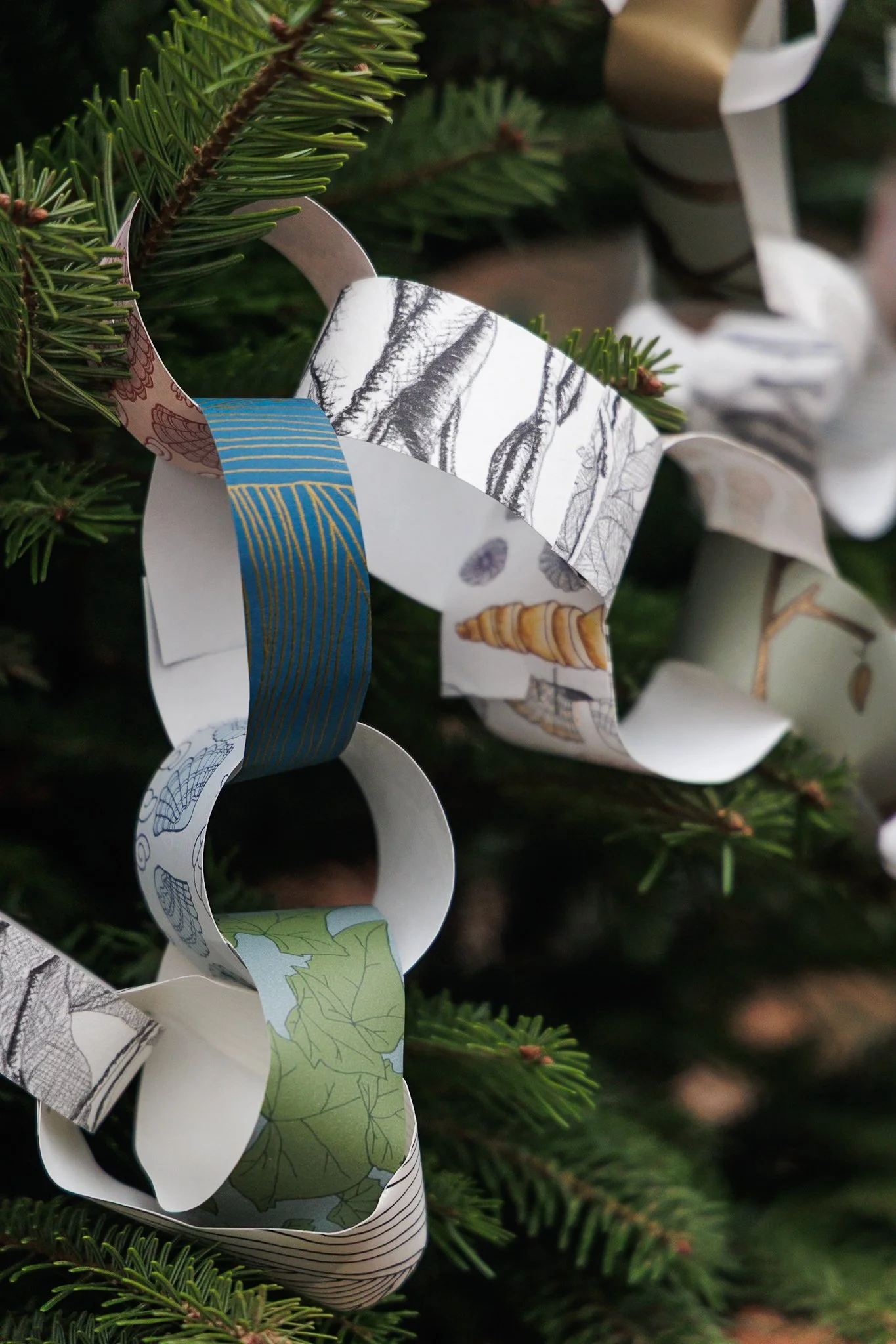 A detail of paper chains made from scraps of mixed patterns of Abigail Edwards wallpaper hanging in a fir tree