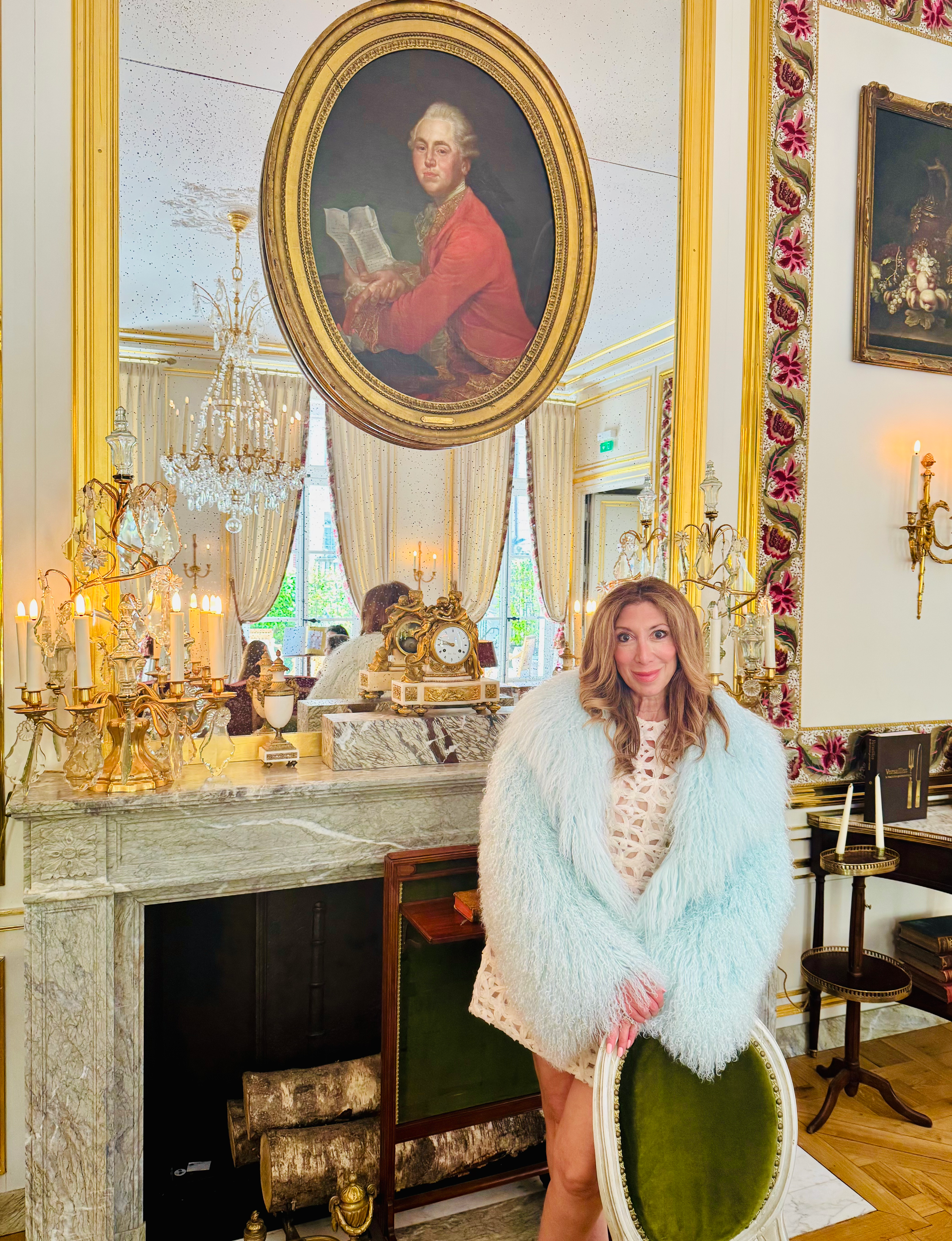 Michele Rosenthal  in an ornate, light-filled room featuring historic gilt moldings, a marble fireplace, and a classic oval portrait